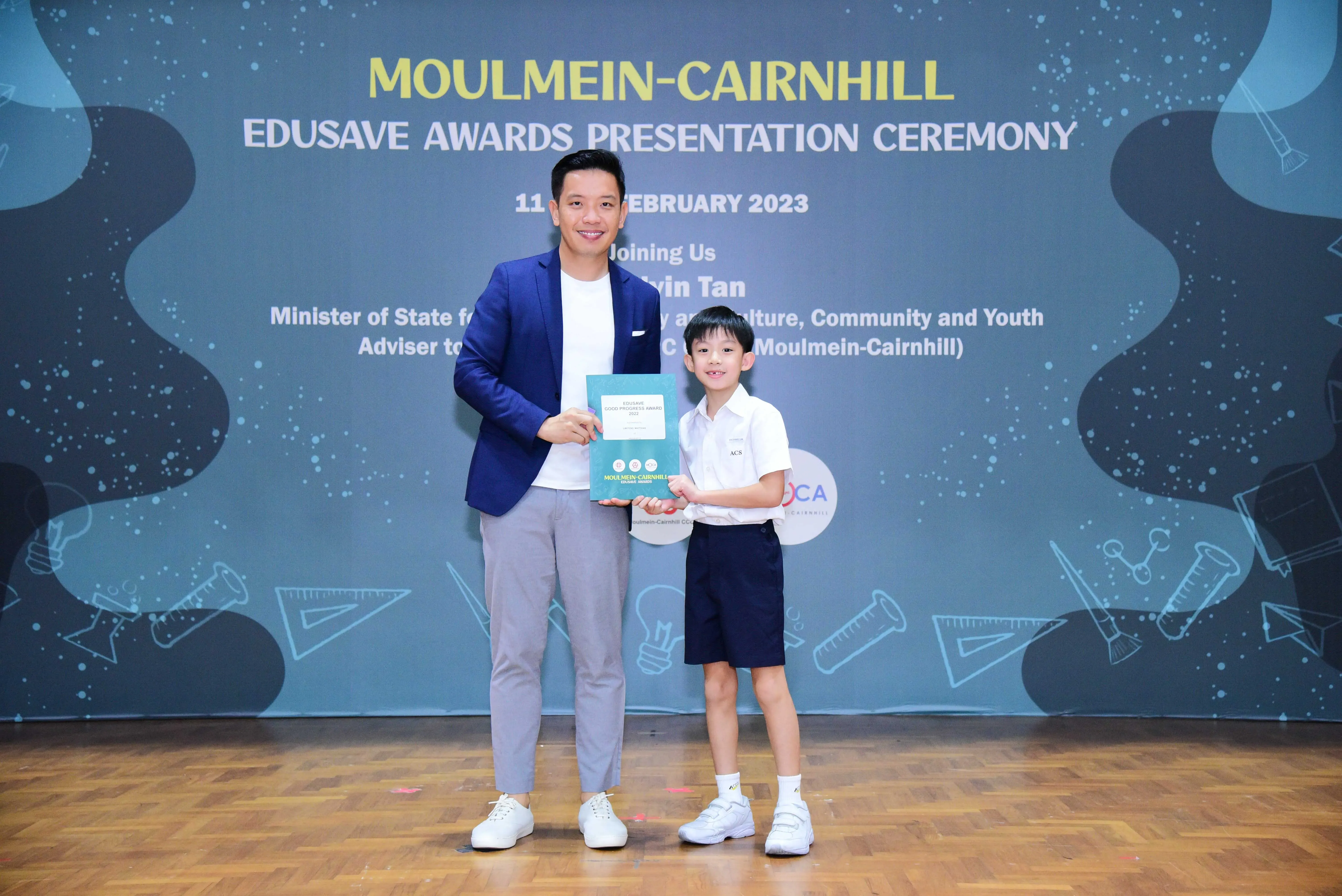 Man in blue blazer and young boy in school uniform hold a certificate at Moulmein-Cairnhill Edusave Awards 2023.