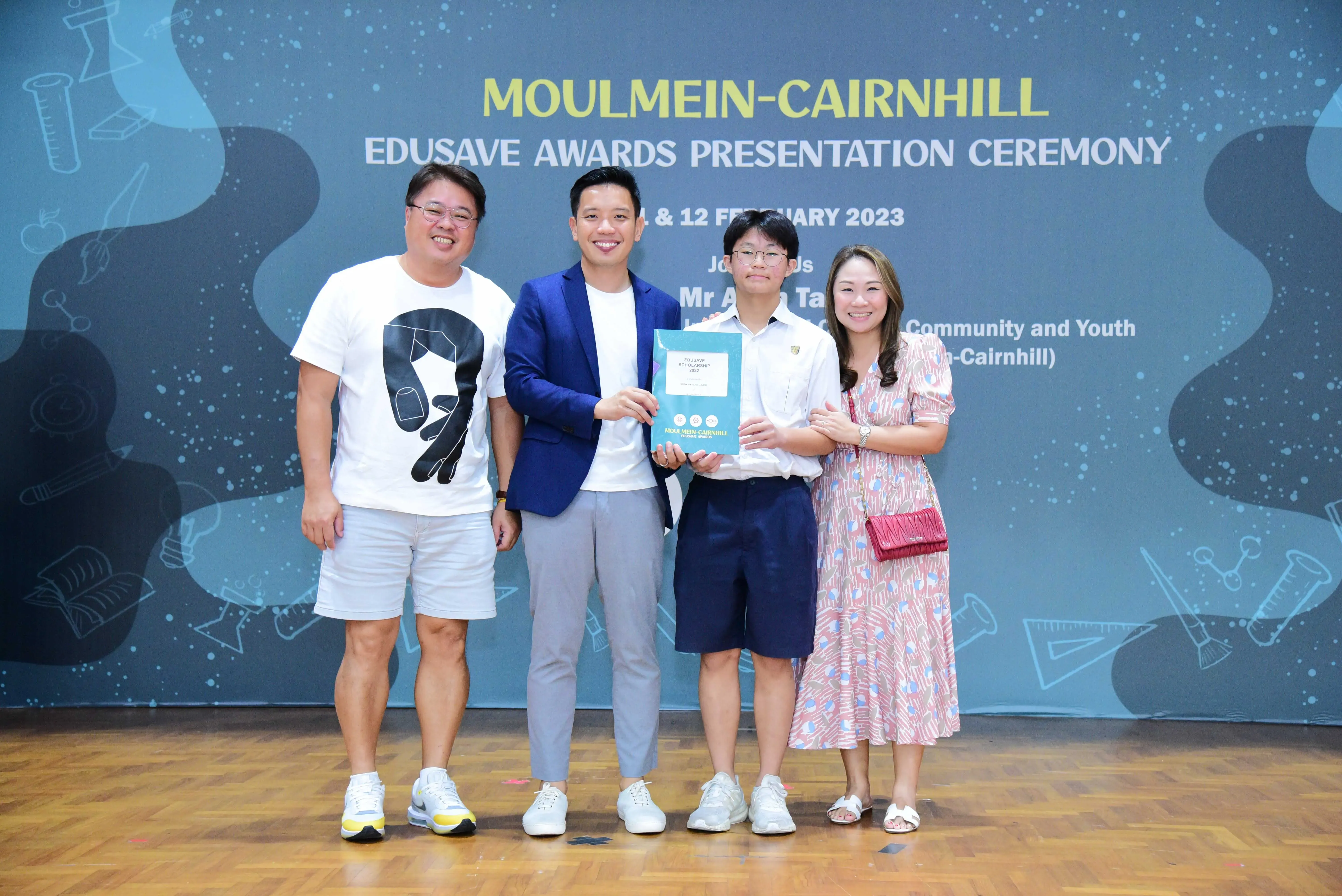Four people pose holding an award booklet at the Moulmein-Cairnhill Edusave Awards Presentation Ceremony 2023.