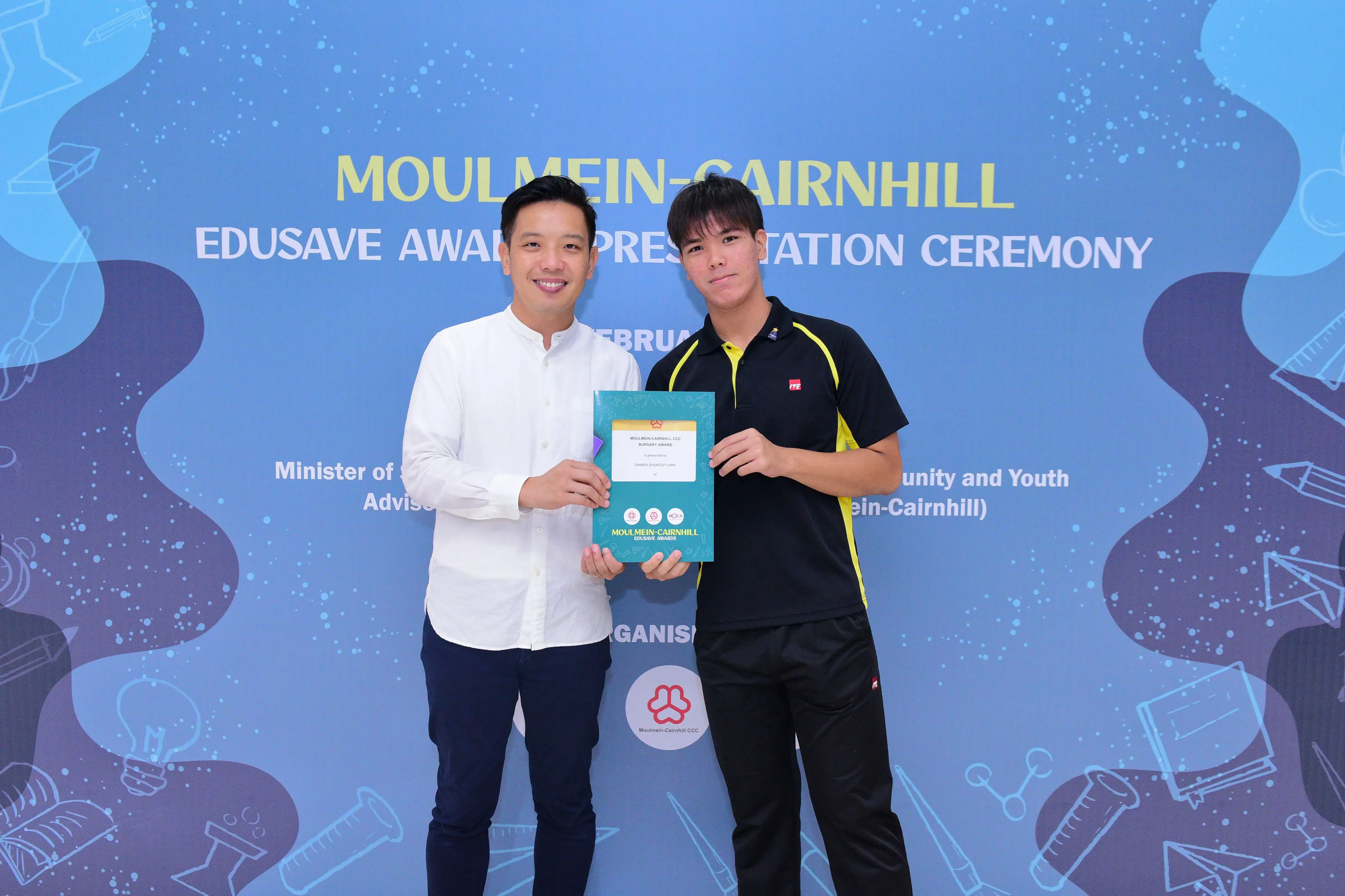 Two men hold a certificate together at the Moulmein-Cairnhill Edusave Award Presentation Ceremony backdrop.