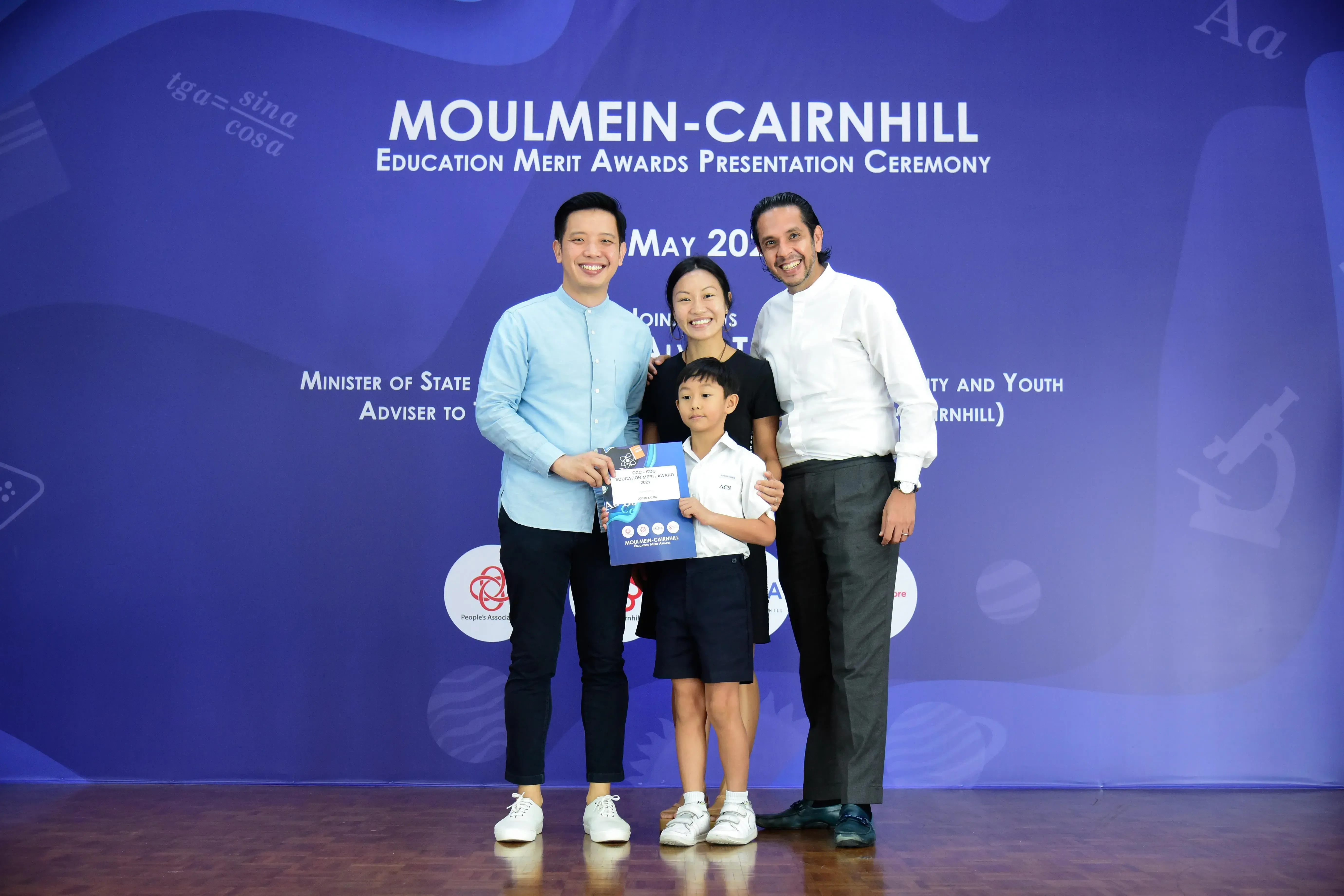 Three adults and a young boy holding a certificate pose at the Moulmein-Cairnhill Education Merit Awards ceremony.