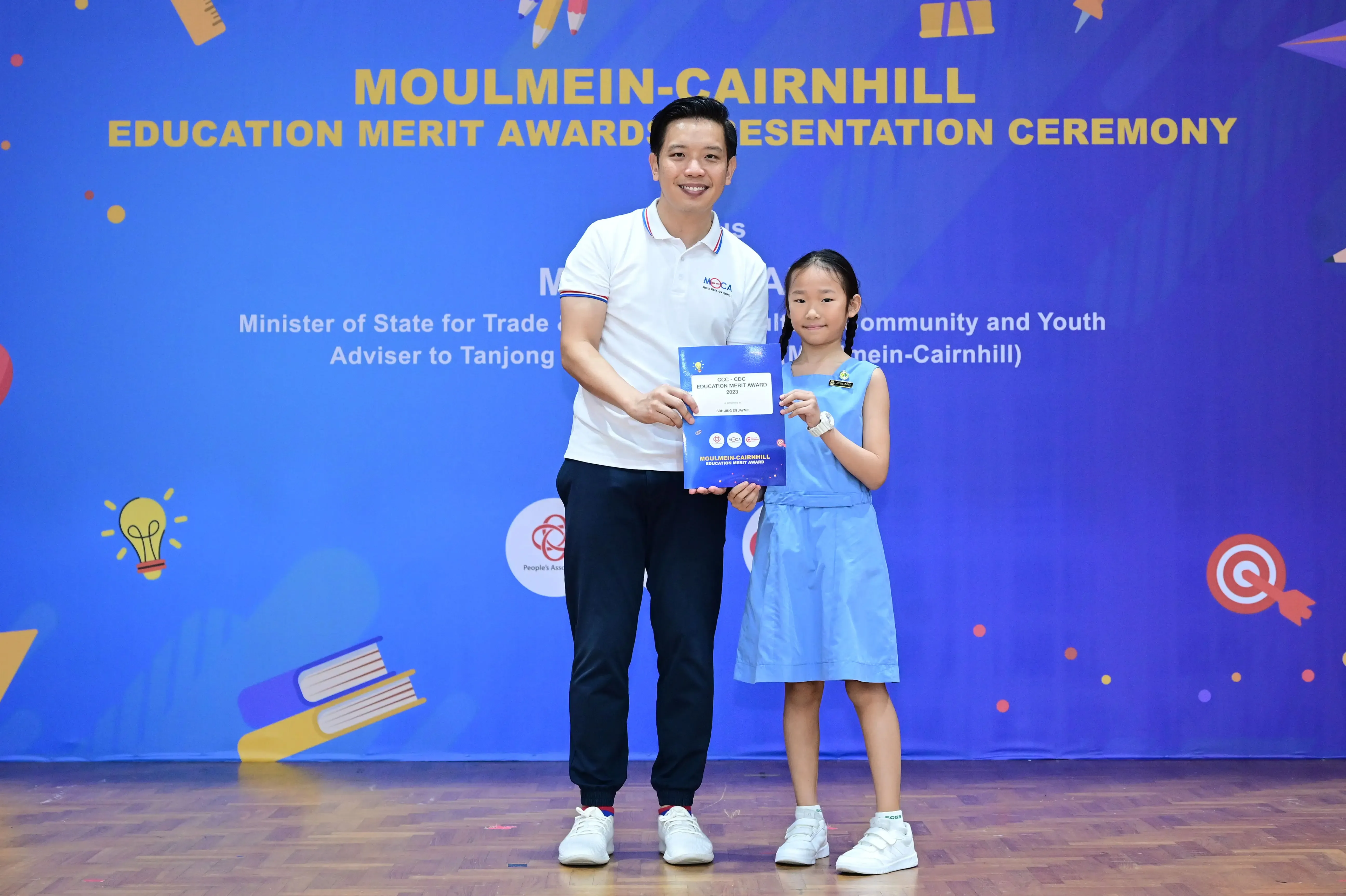 Man and young girl hold a blue award certificate at the Moulmein-Cairnhill Education Merit Award Presentation Ceremony.