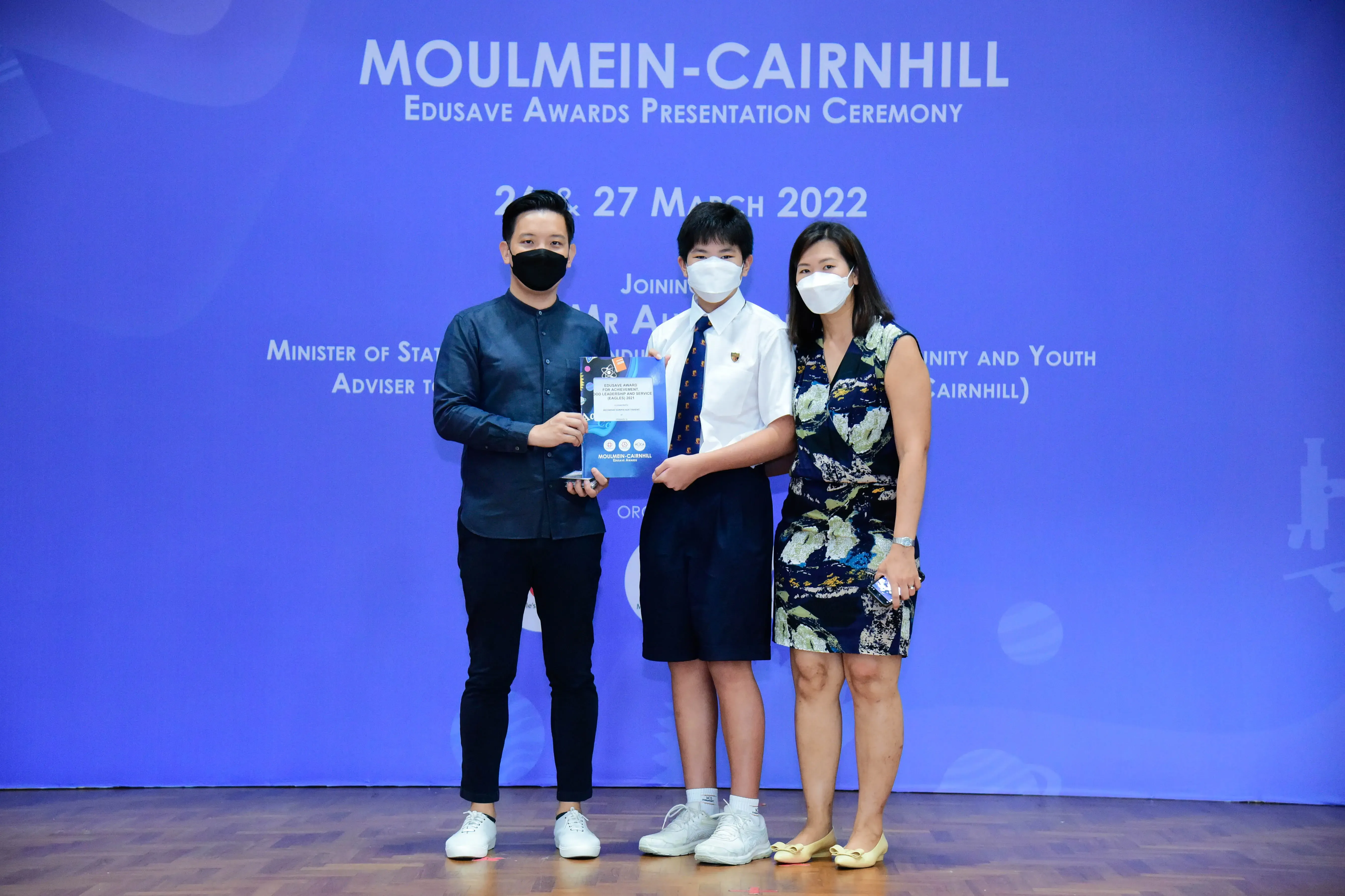 Three masked people pose with an award at the Moulmein-Cairnhill Edusave Awards Presentation Ceremony, March 2022.