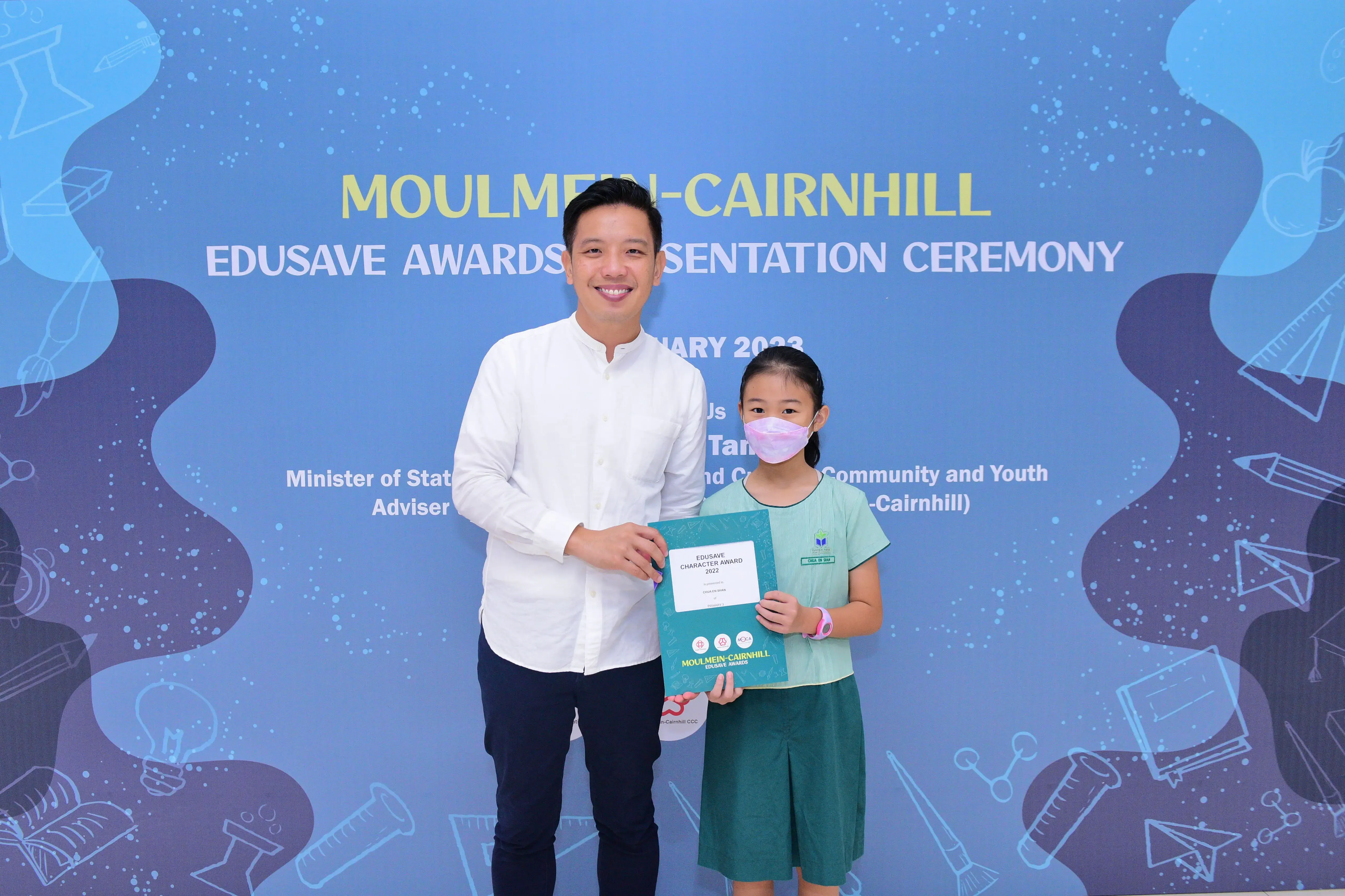 A man and a young girl hold an Edusave Character Award certificate at the Moulmein-Cairnhill awards ceremony.