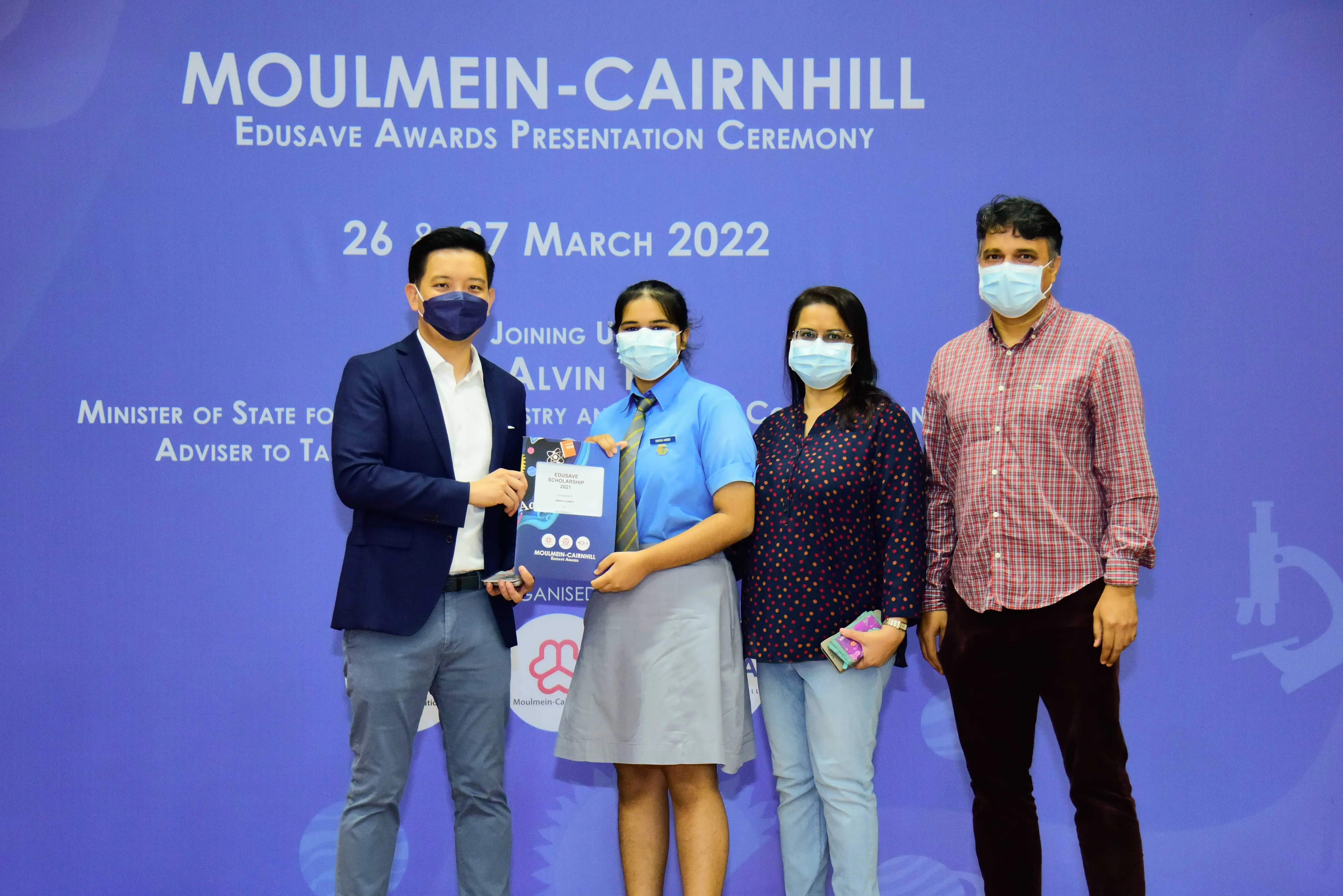 Four masked people pose at the Moulmein-Cairnhill Edusave Awards Ceremony on 26-27 March 2022, holding an award.