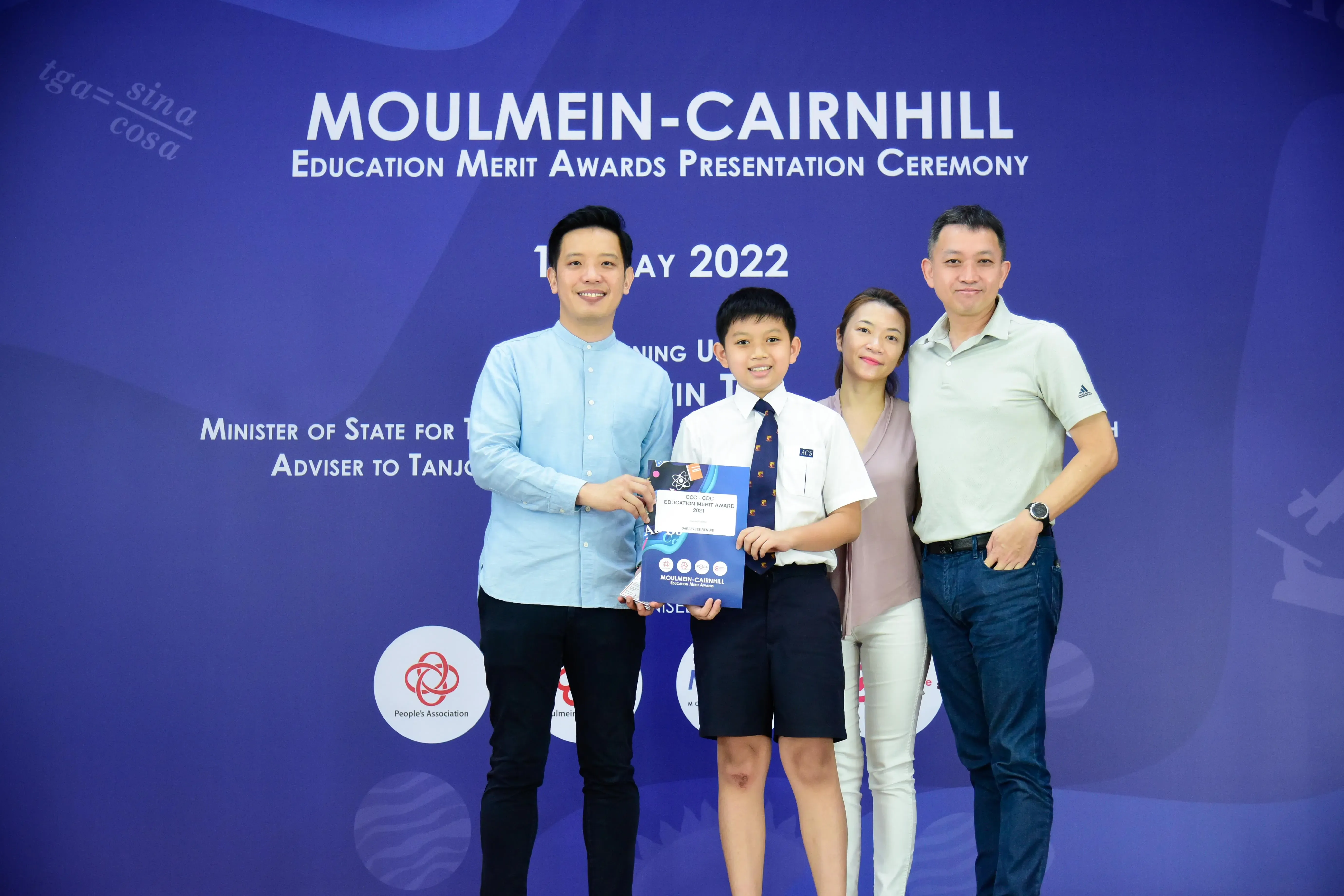 Four people pose at the 2022 Moulmein-Cairnhill Education Merit Awards, with a boy holding an award certificate.