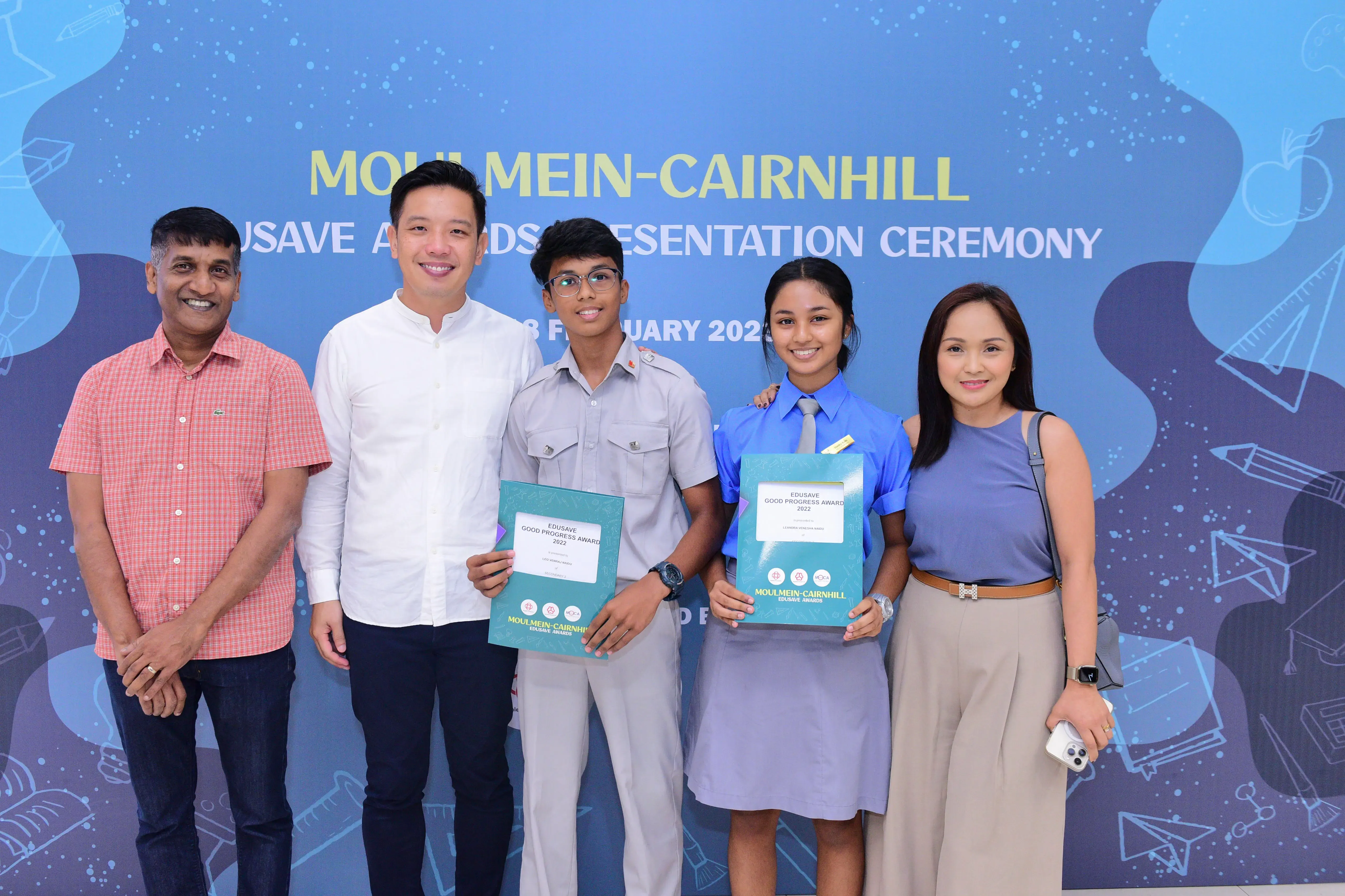 Five people pose at the Moulmein-Cairnhill Edusave Awards Presentation Ceremony, with two students holding award certificates.