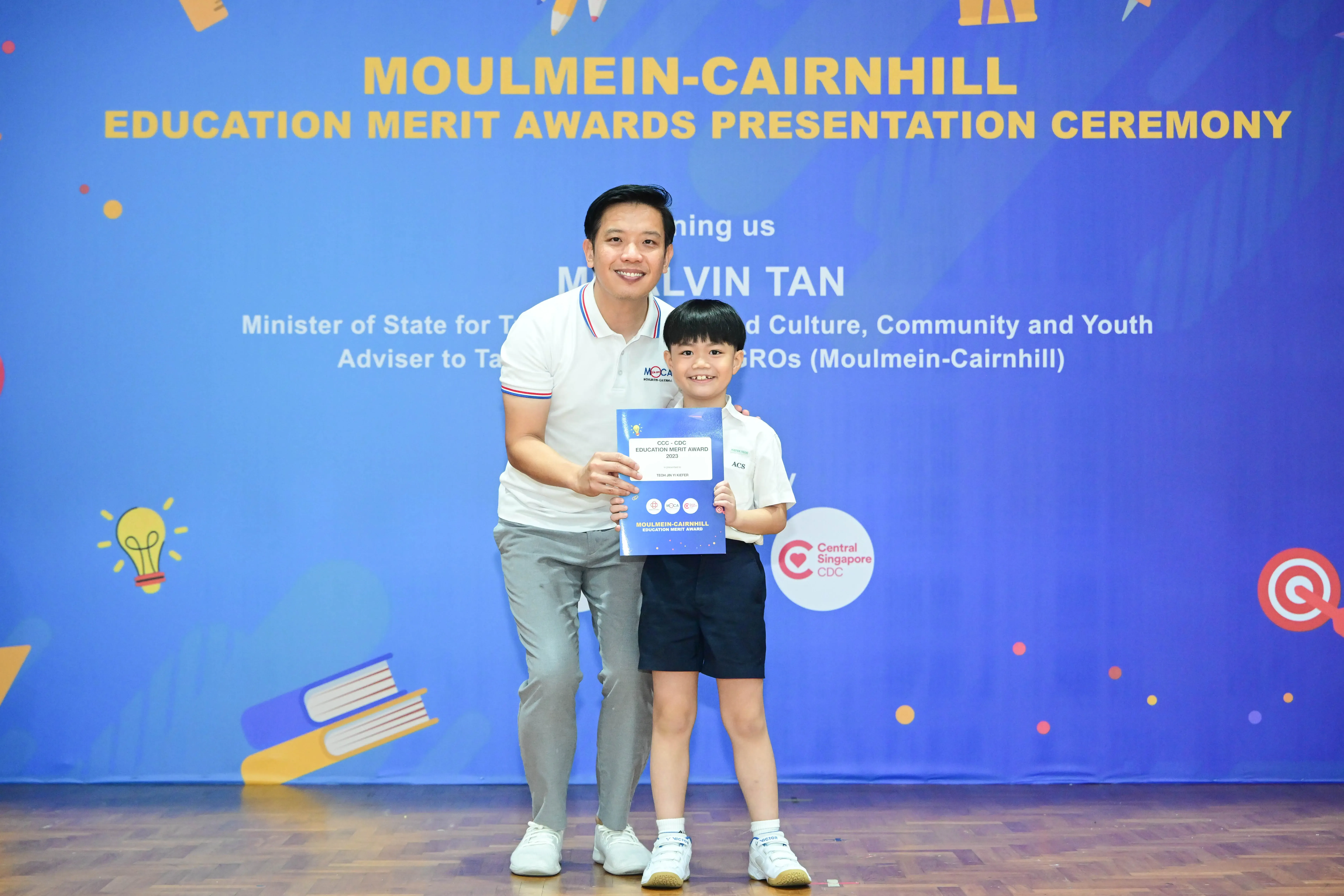 A man and a young boy hold an award certificate at the Moulmein-Cairnhill Education Merit Awards Presentation Ceremony.