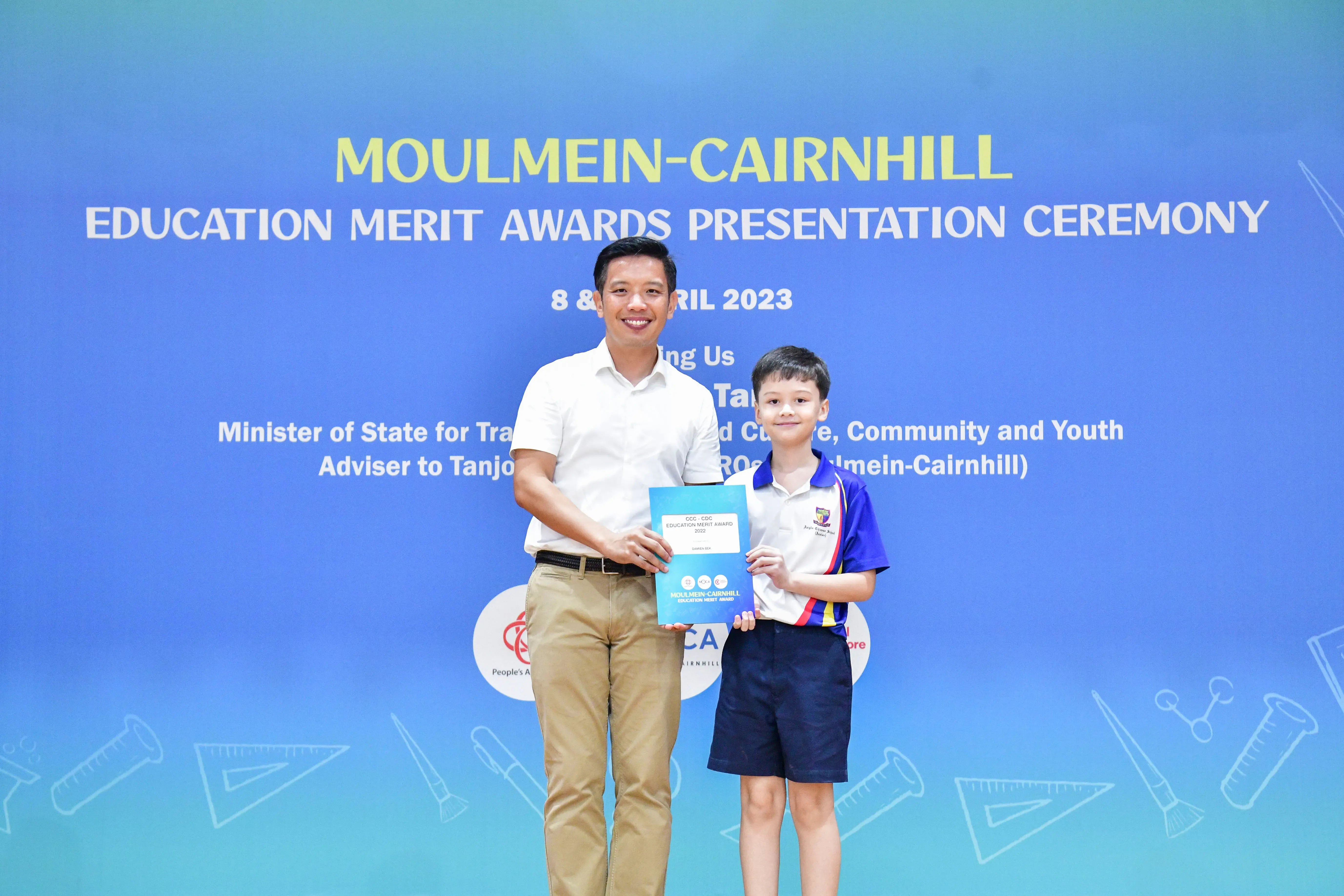 A man and a young boy hold a blue award certificate at the Moulmein-Cairnhill Education Merit Awards 2023.