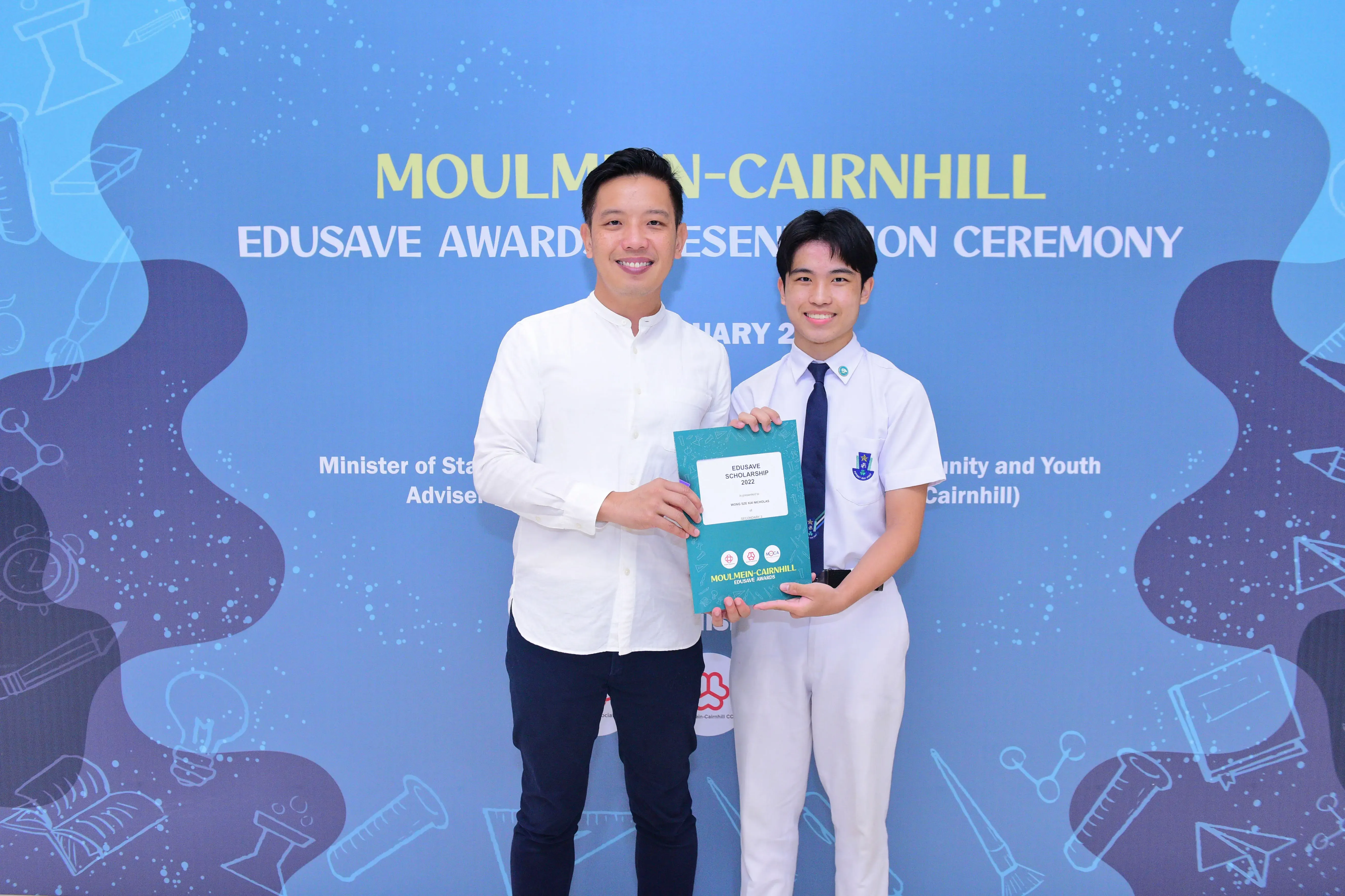 Two men smile holding an Edusave Scholarship award at the Moulmein-Cairnhill Edusave Awards Presentation Ceremony.