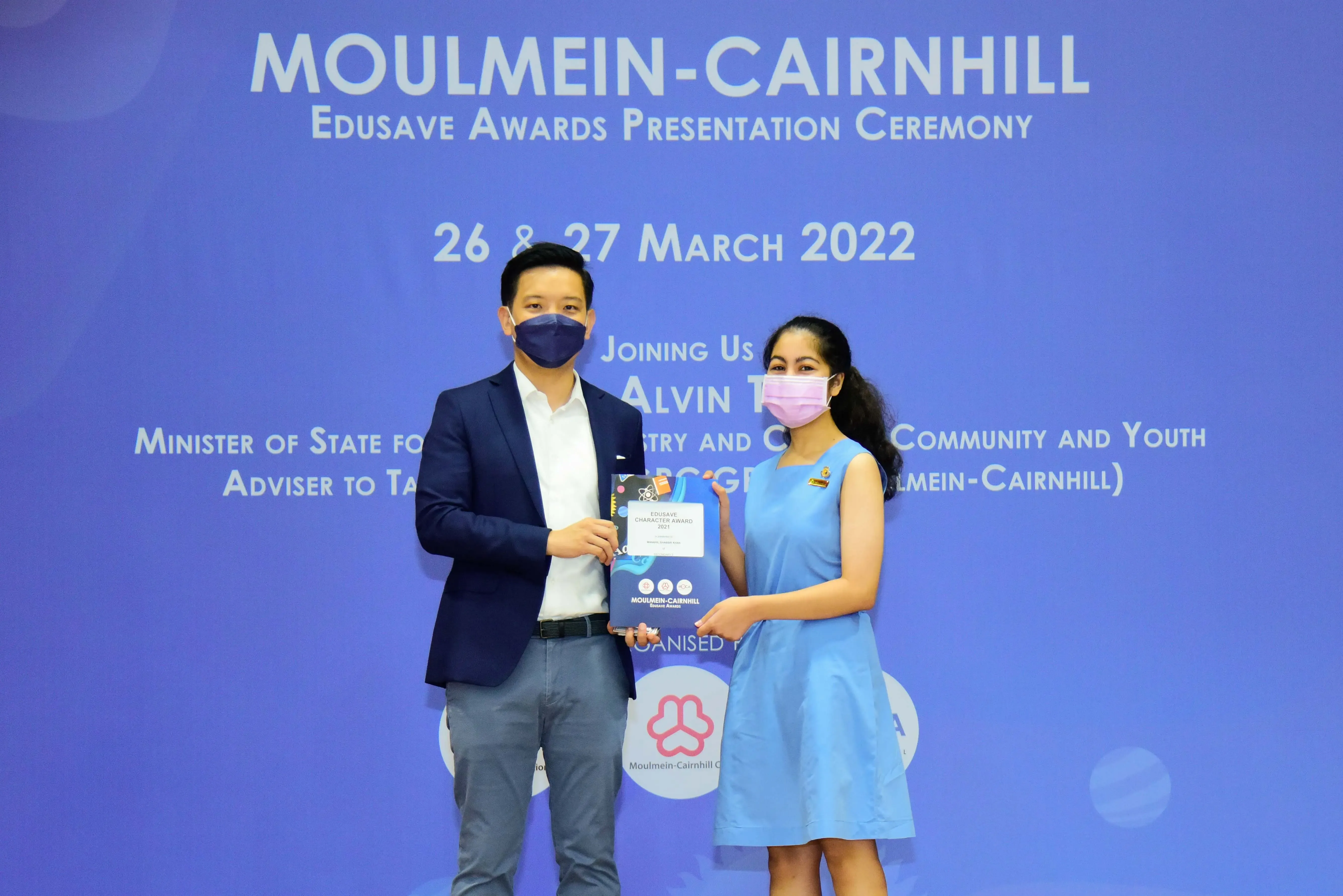 Two masked individuals hold an award together at the Moulmein-Cairnhill Edusave Awards Ceremony, March 2022.