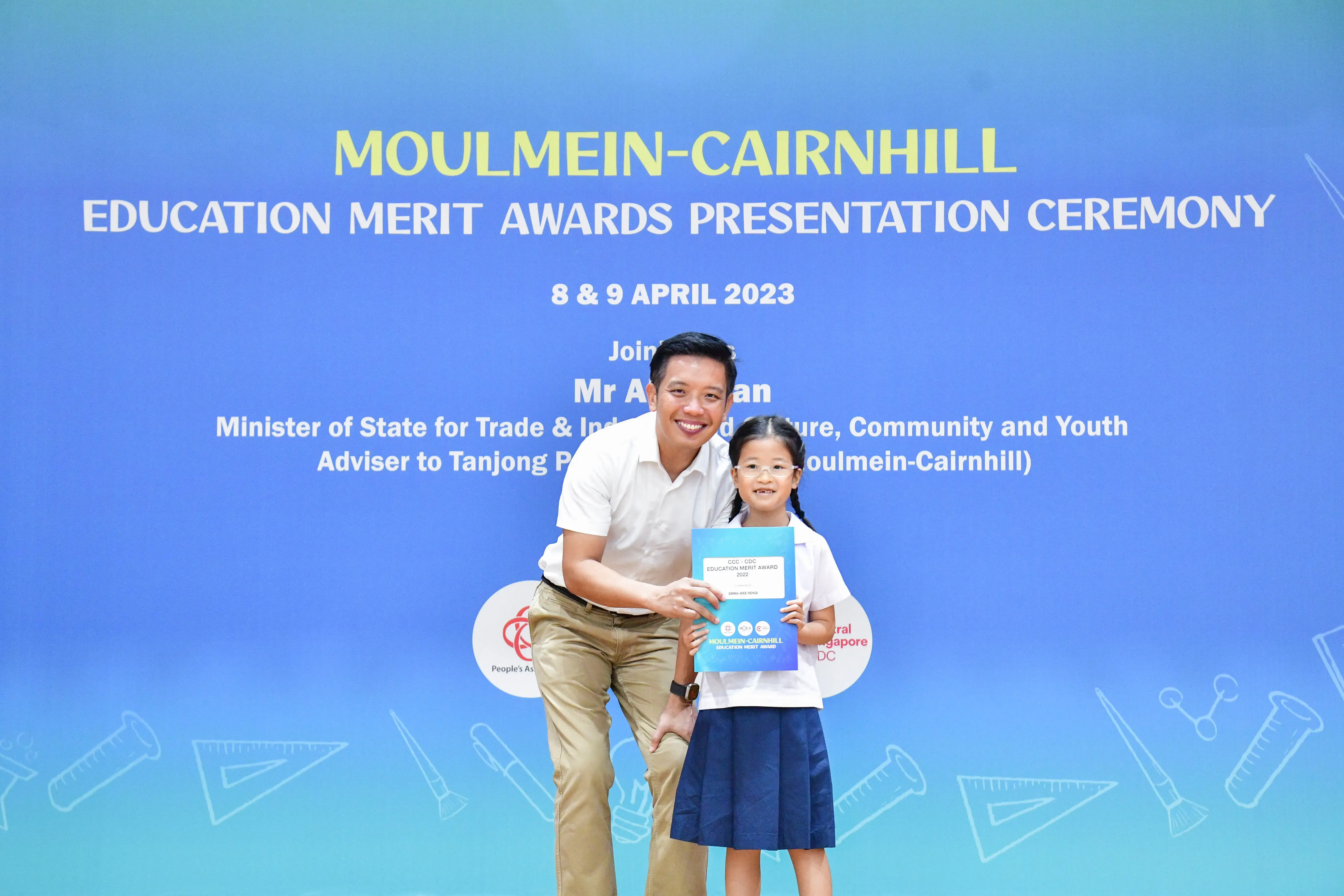 A man and a young girl hold an award certificate at the Moulmein-Cairnhill Education Merit Awards Ceremony, April 2023.