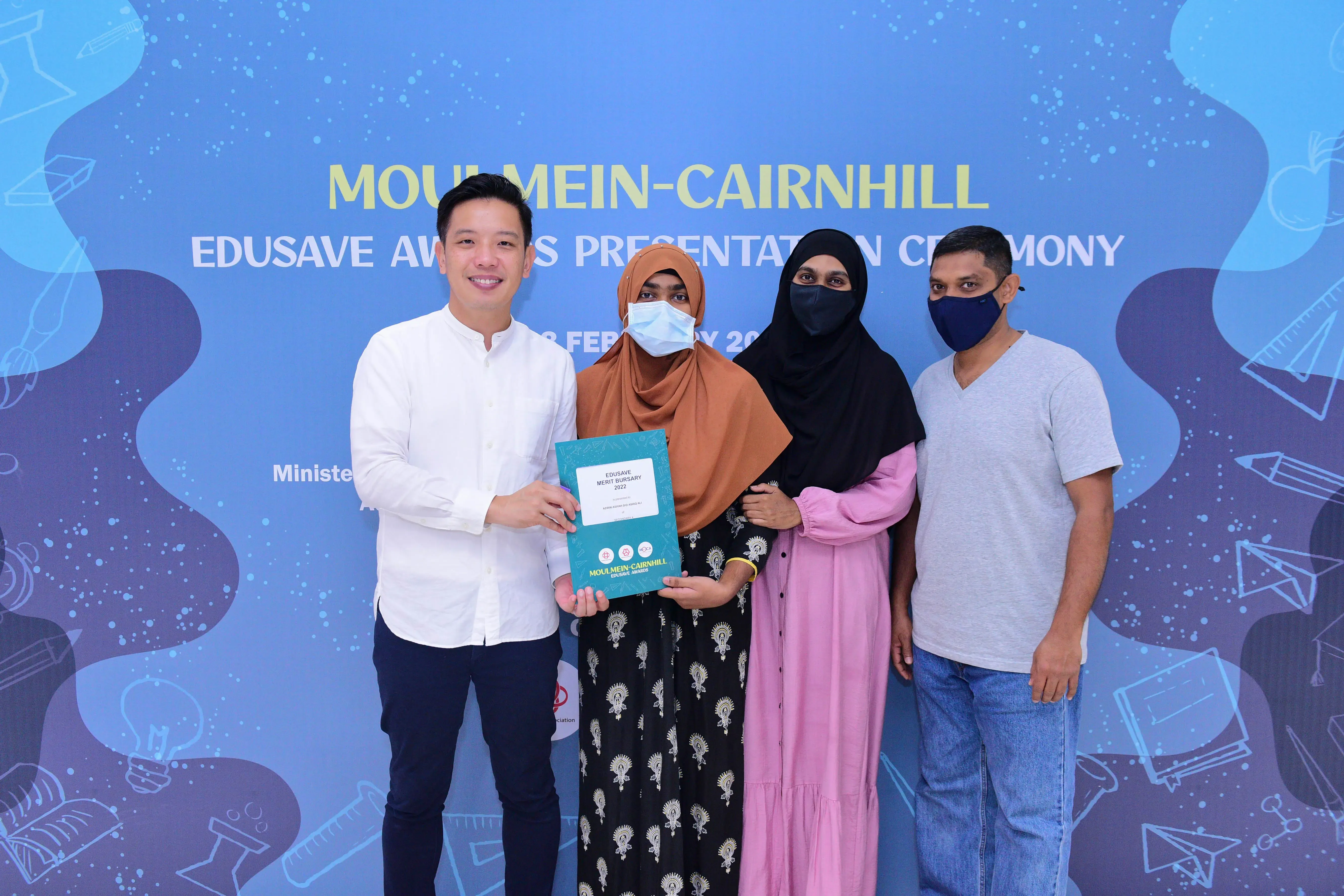 Four people wearing masks pose at the Moulmein-Cairnhill Edusave Awards Presentation Ceremony, holding a certificate.
