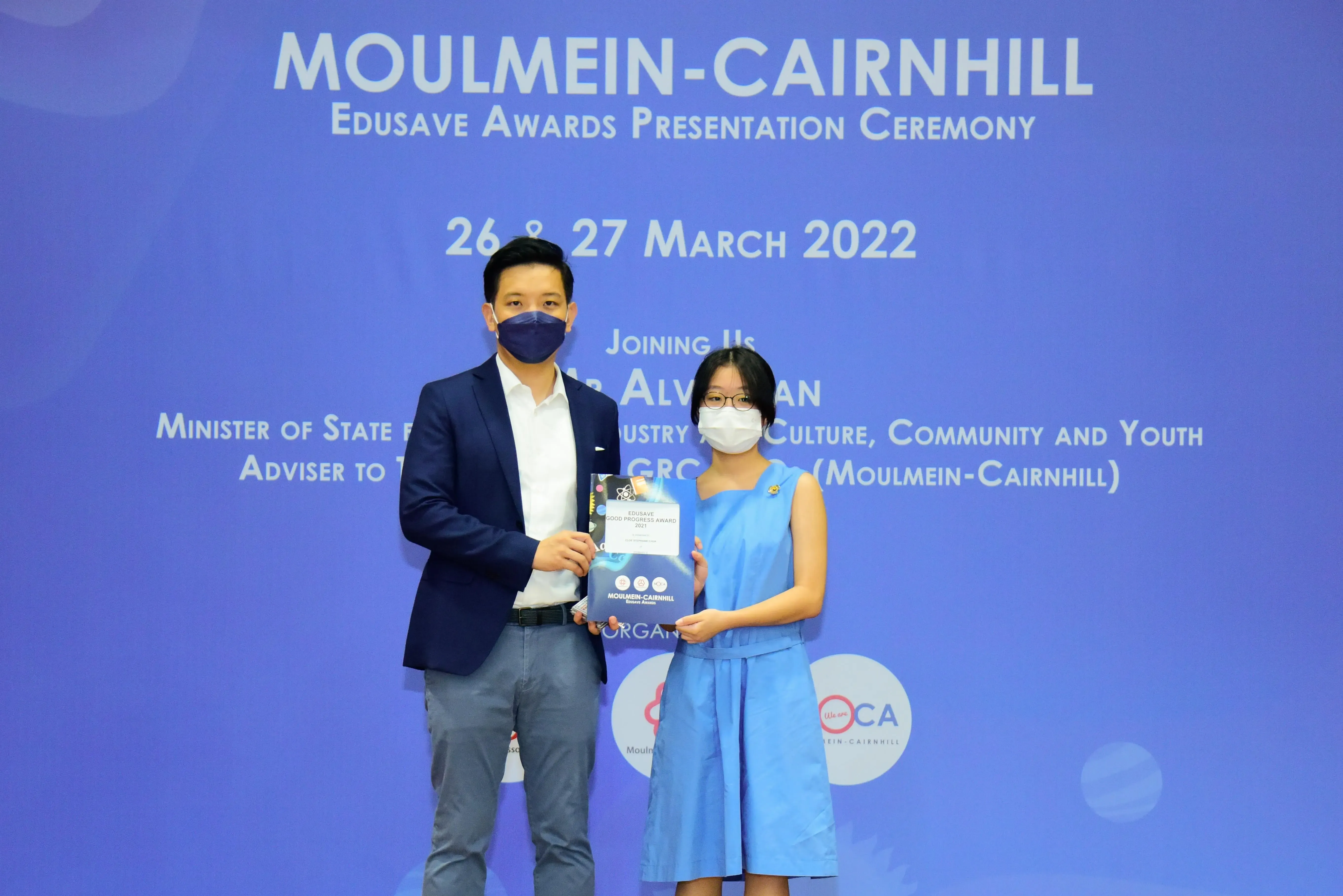 Two masked individuals hold an award at the Moulmein-Cairnhill Edusave Awards Presentation Ceremony, March 2022.