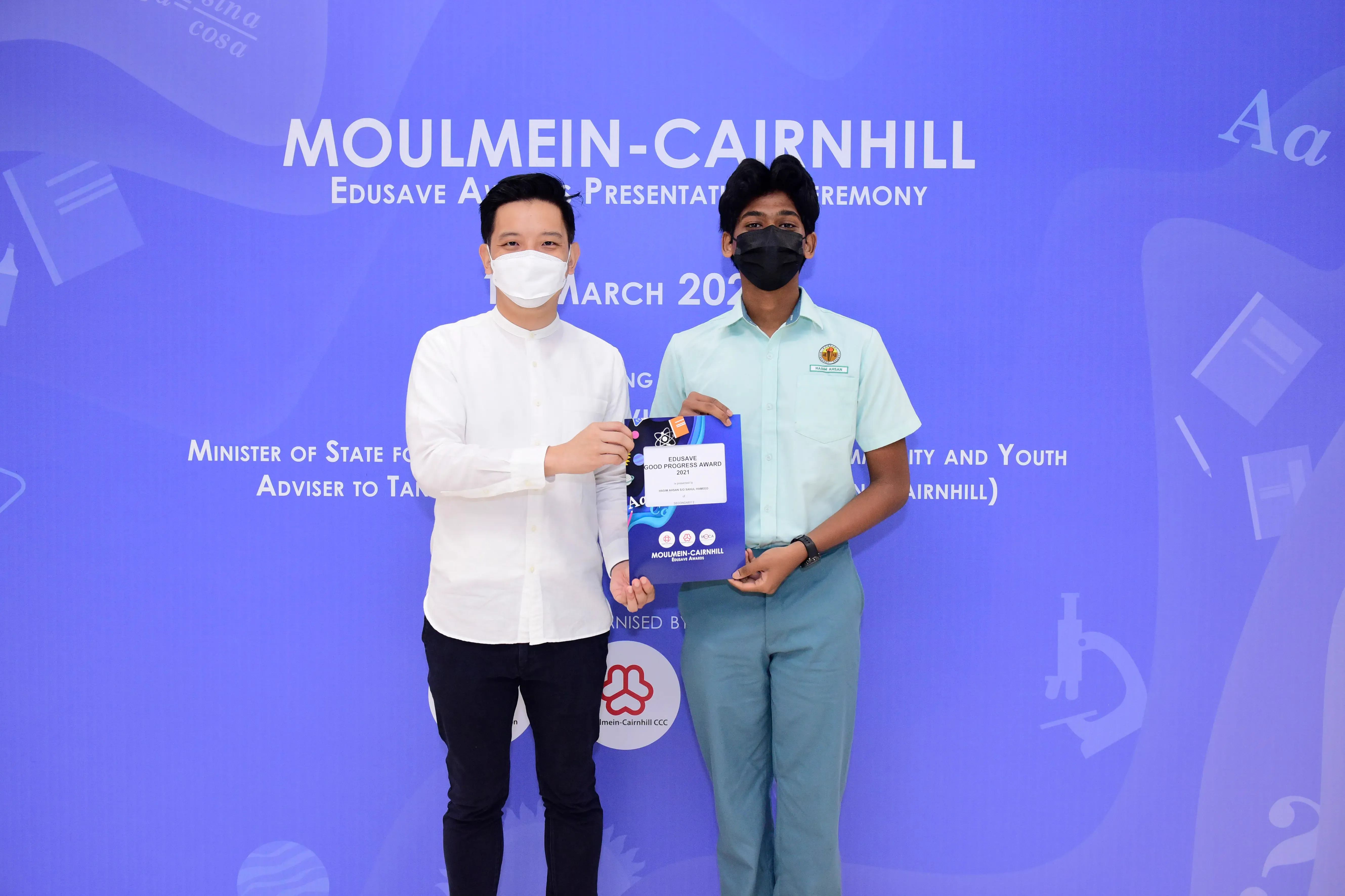 Two masked individuals hold an Edusave Good Progress Award bag at the Moulmein-Cairnhill award ceremony.