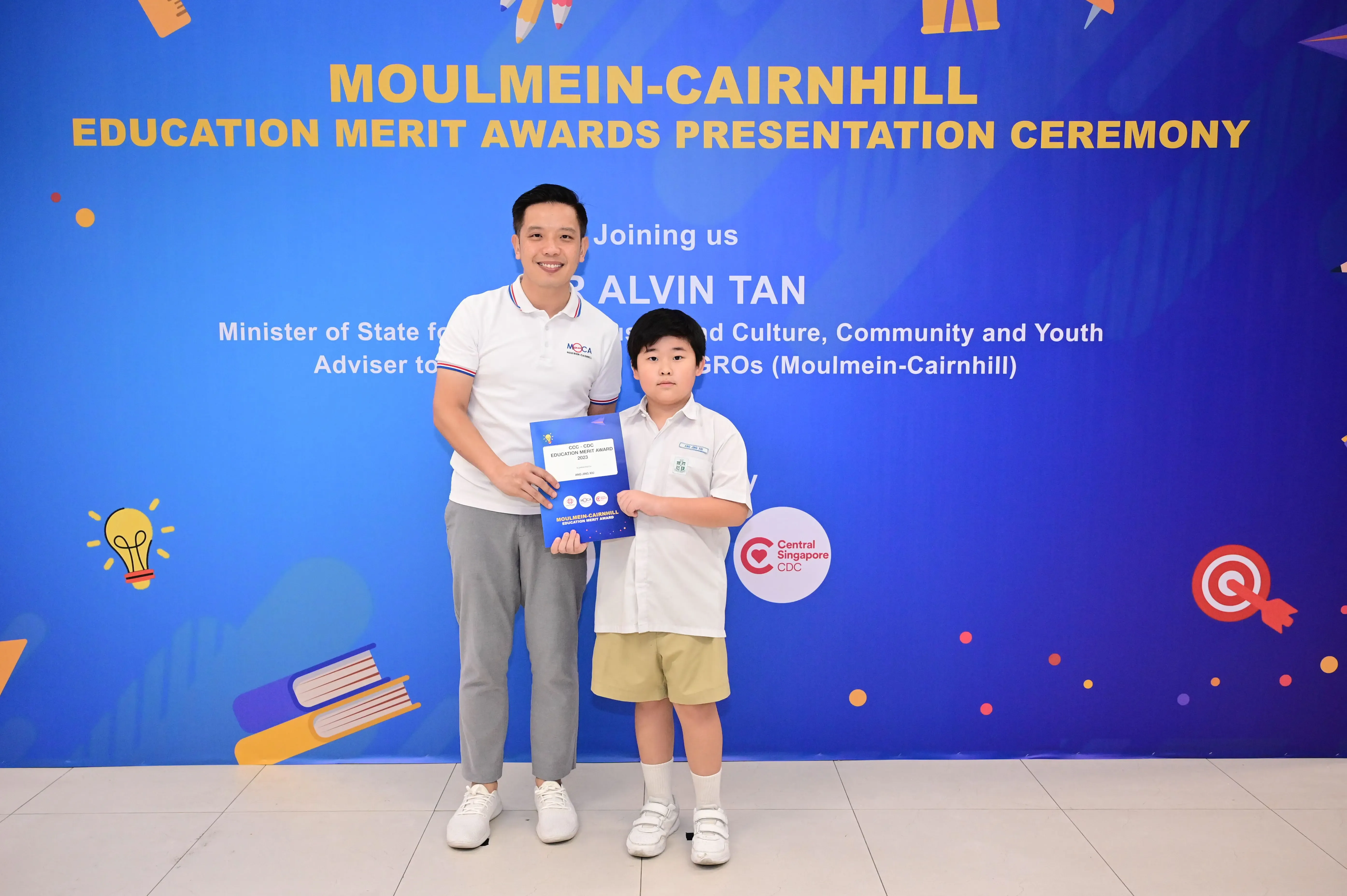 Adult and young boy holding a merit award certificate at the Moulmein-Cairnhill Education Merit Awards Presentation Ceremony.
