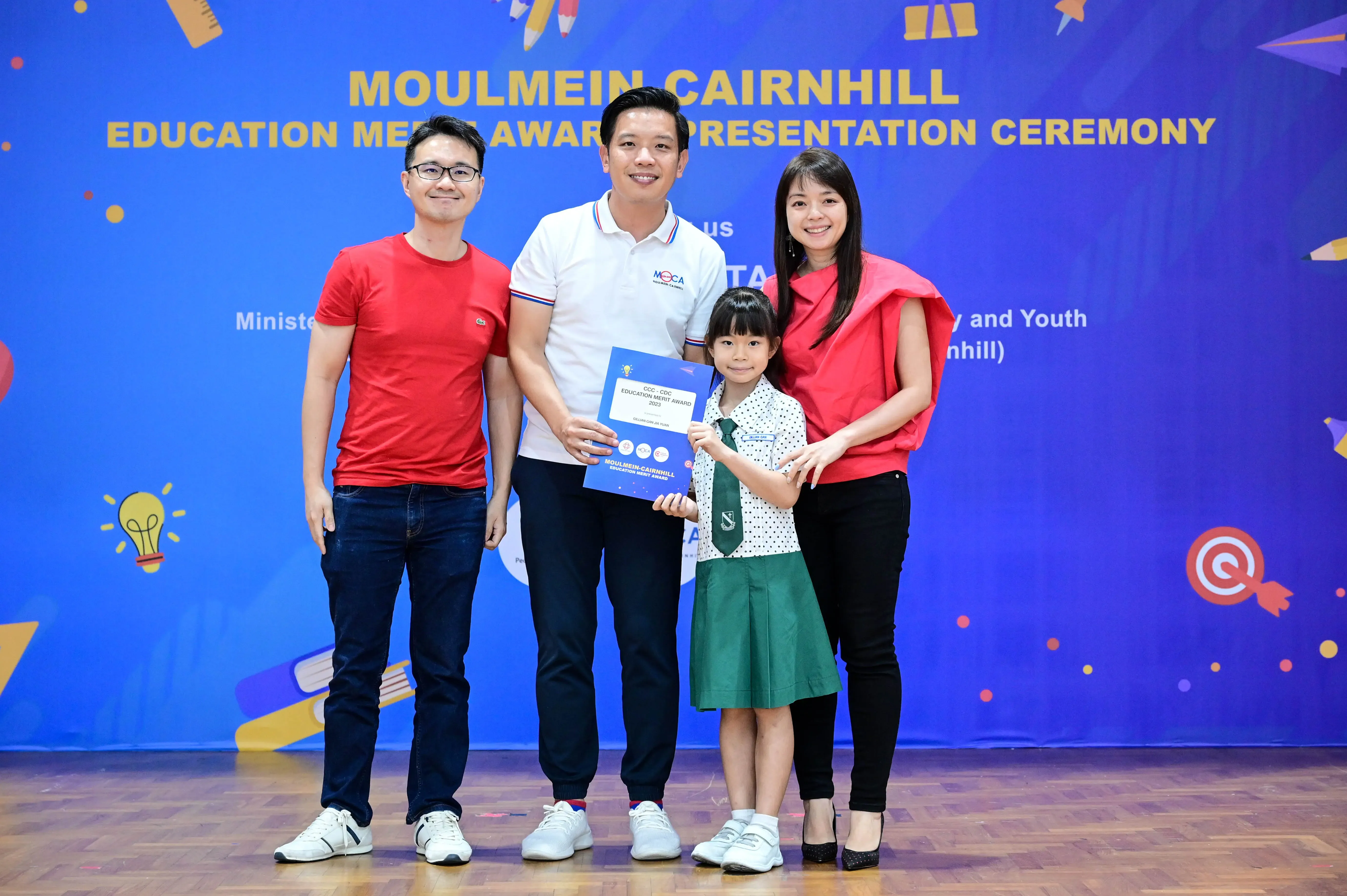 Three adults and a young girl in school uniform hold a certificate at Moulmein Cairnhill Education Merit Award ceremony.