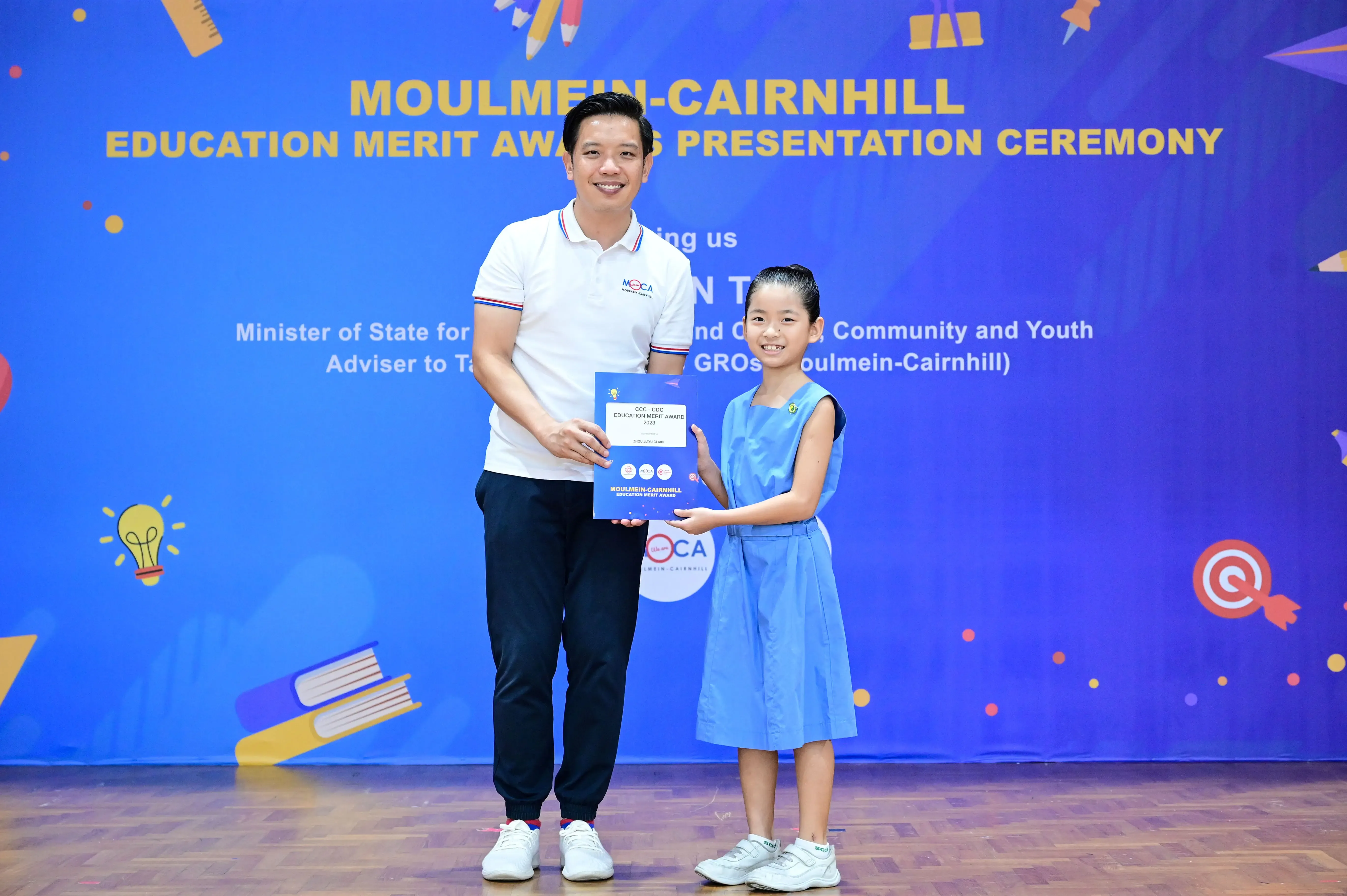 A man and a young girl hold a certificate at the Moulmein-Cairnhill Education Merit Awards Presentation Ceremony.