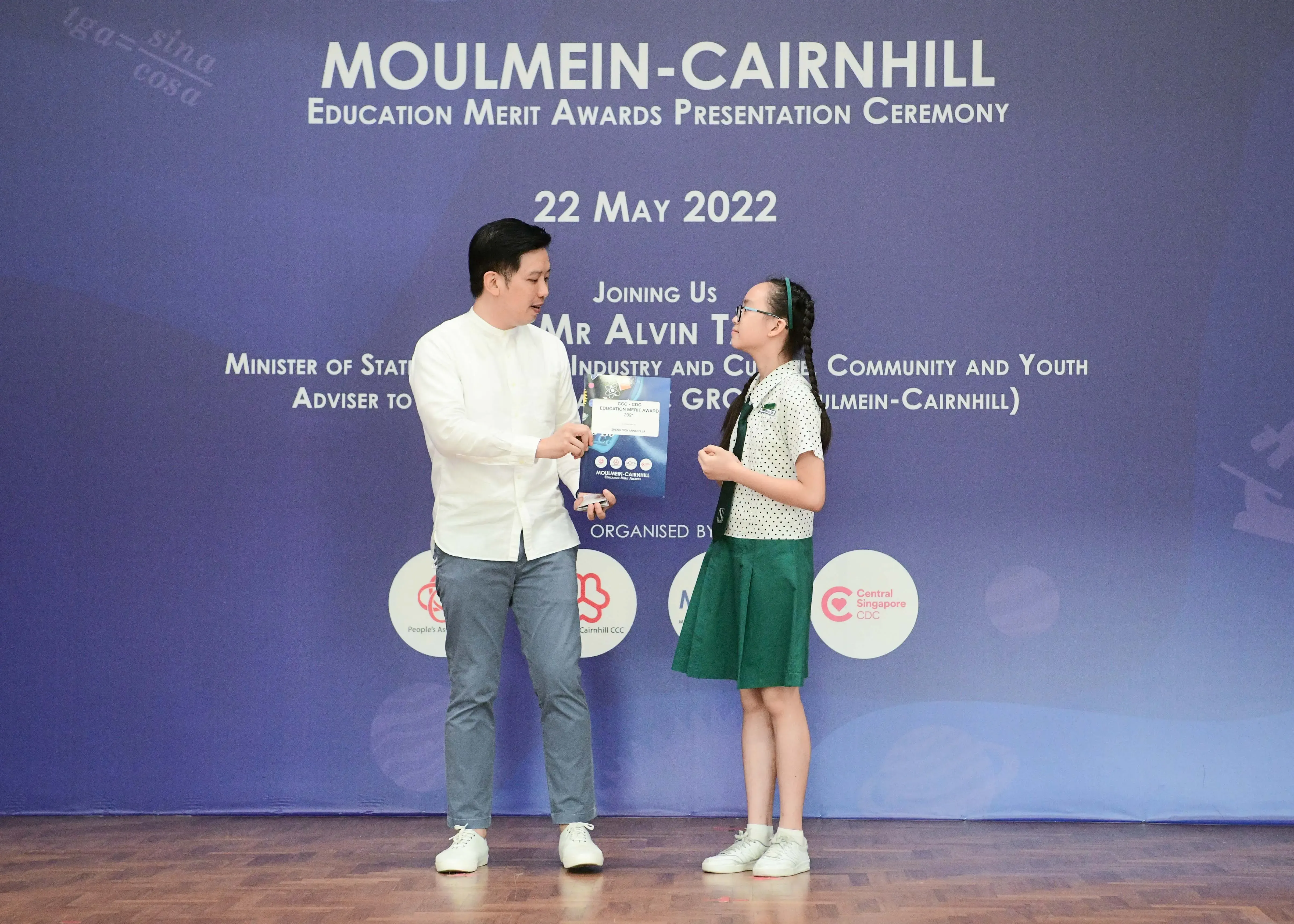 Man in white shirt presents award to young girl in school uniform at Moulmein-Cairnhill Education Merit Awards, May 2022.
