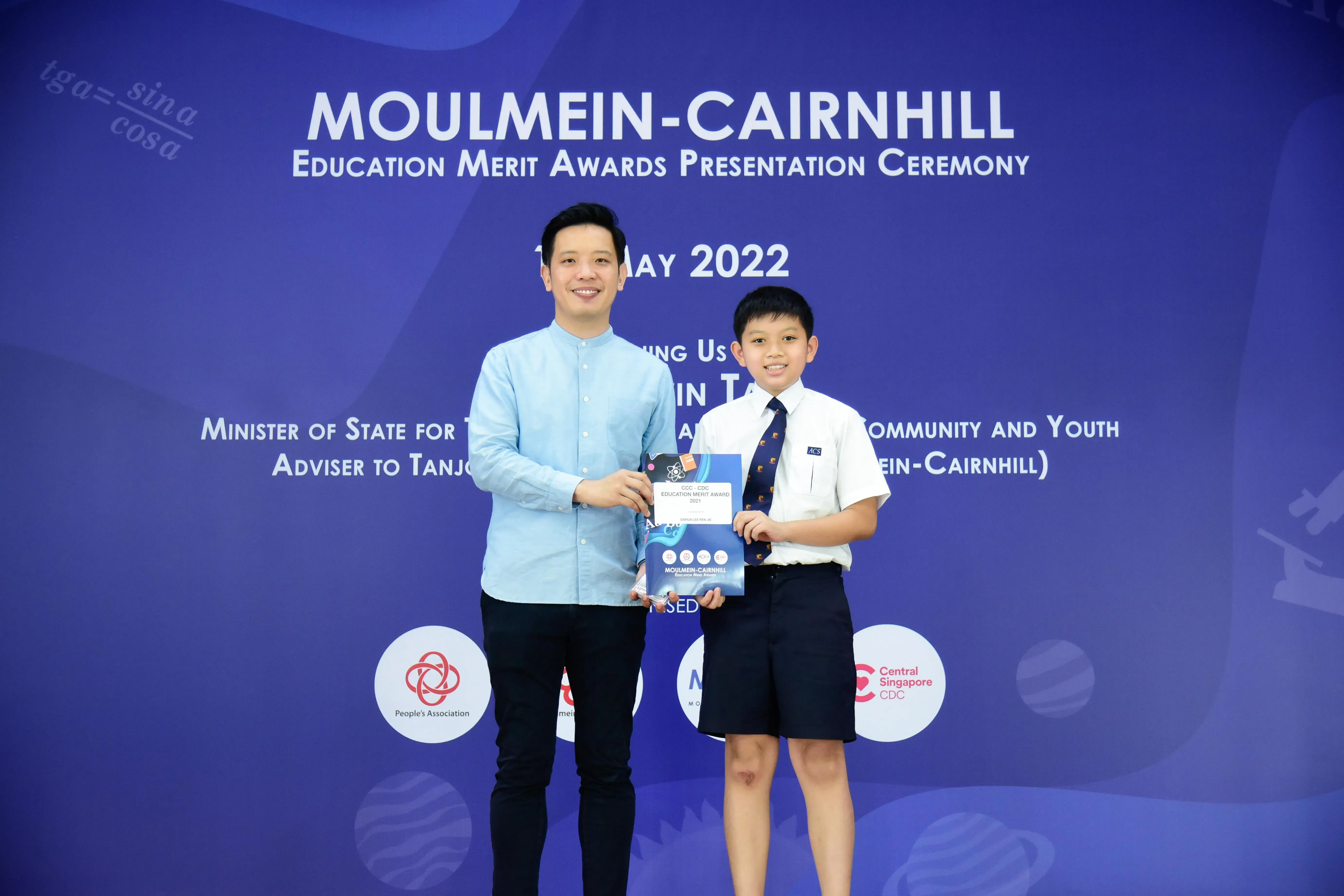 A man and a young boy in school uniform hold an award certificate at the Moulmein-Cairnhill Education Merit Awards 2022.