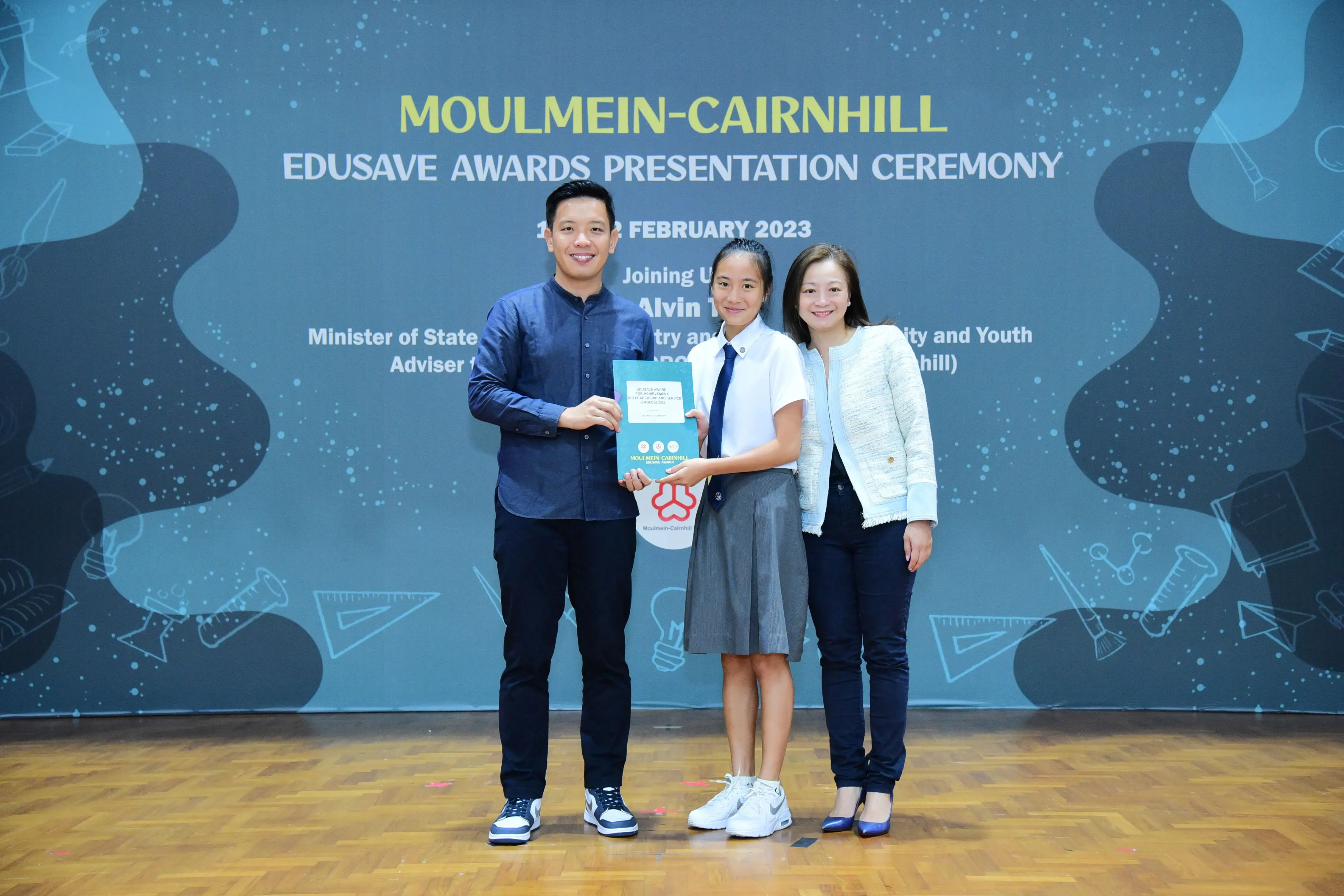 Three people pose together holding a certificate at the Moulmein-Cairnhill Edusave Awards Presentation Ceremony, February 2023.