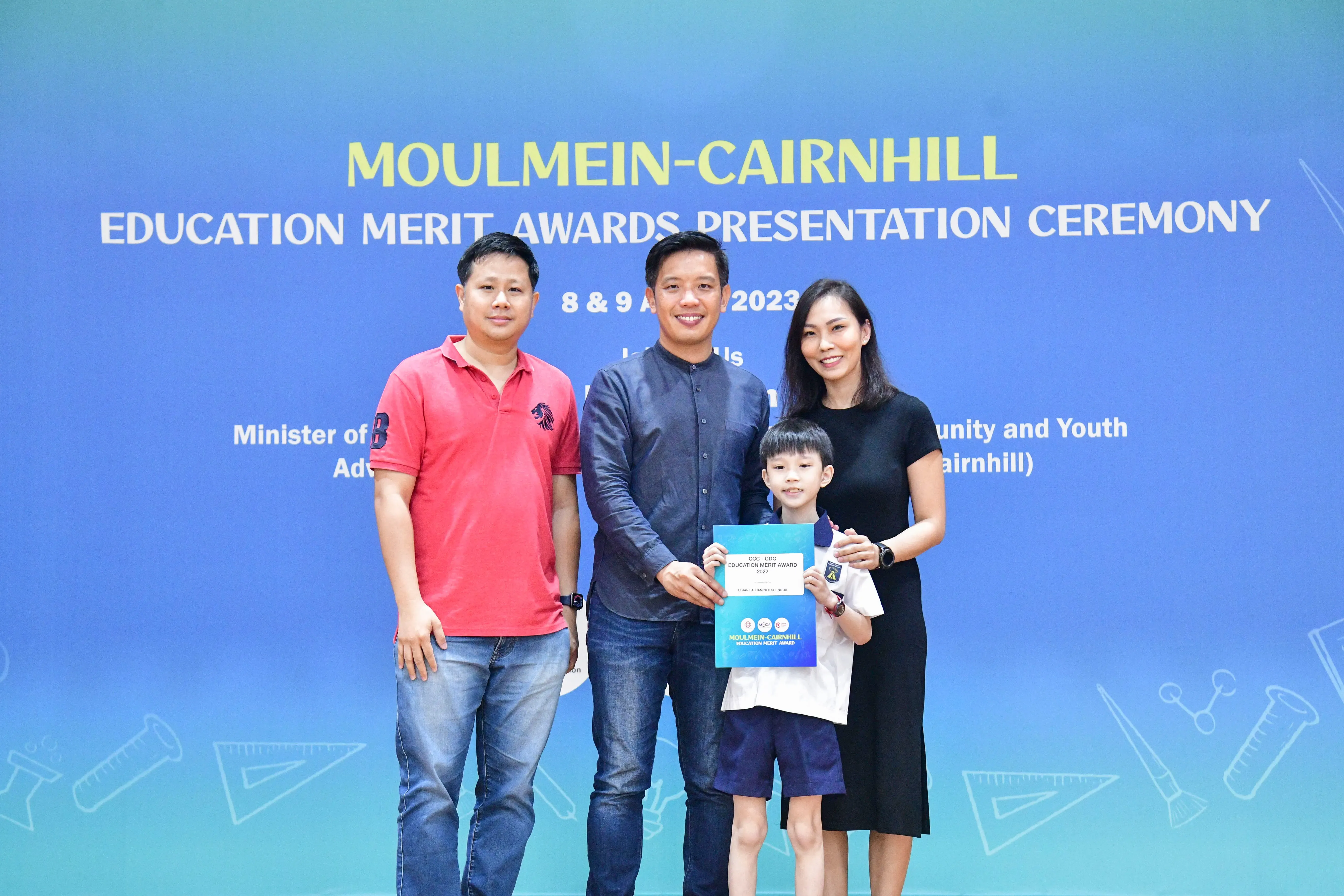 Three adults and a young boy pose with an award certificate at the Moulmein-Cairnhill Education Merit Awards Ceremony 2023.