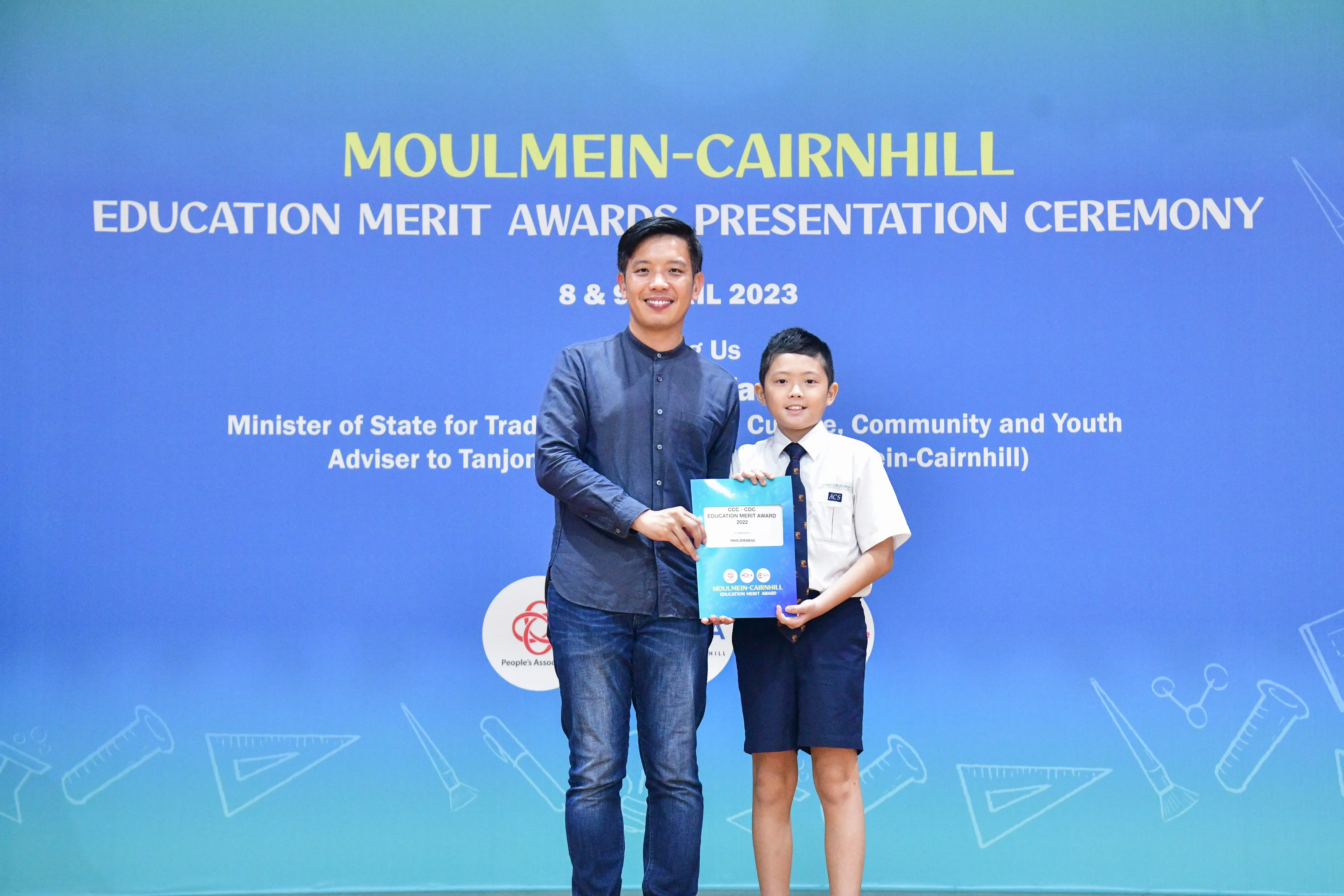 Adult and young boy holding an award certificate at the Moulmein-Cairnhill Education Merit Awards Ceremony 2023.
