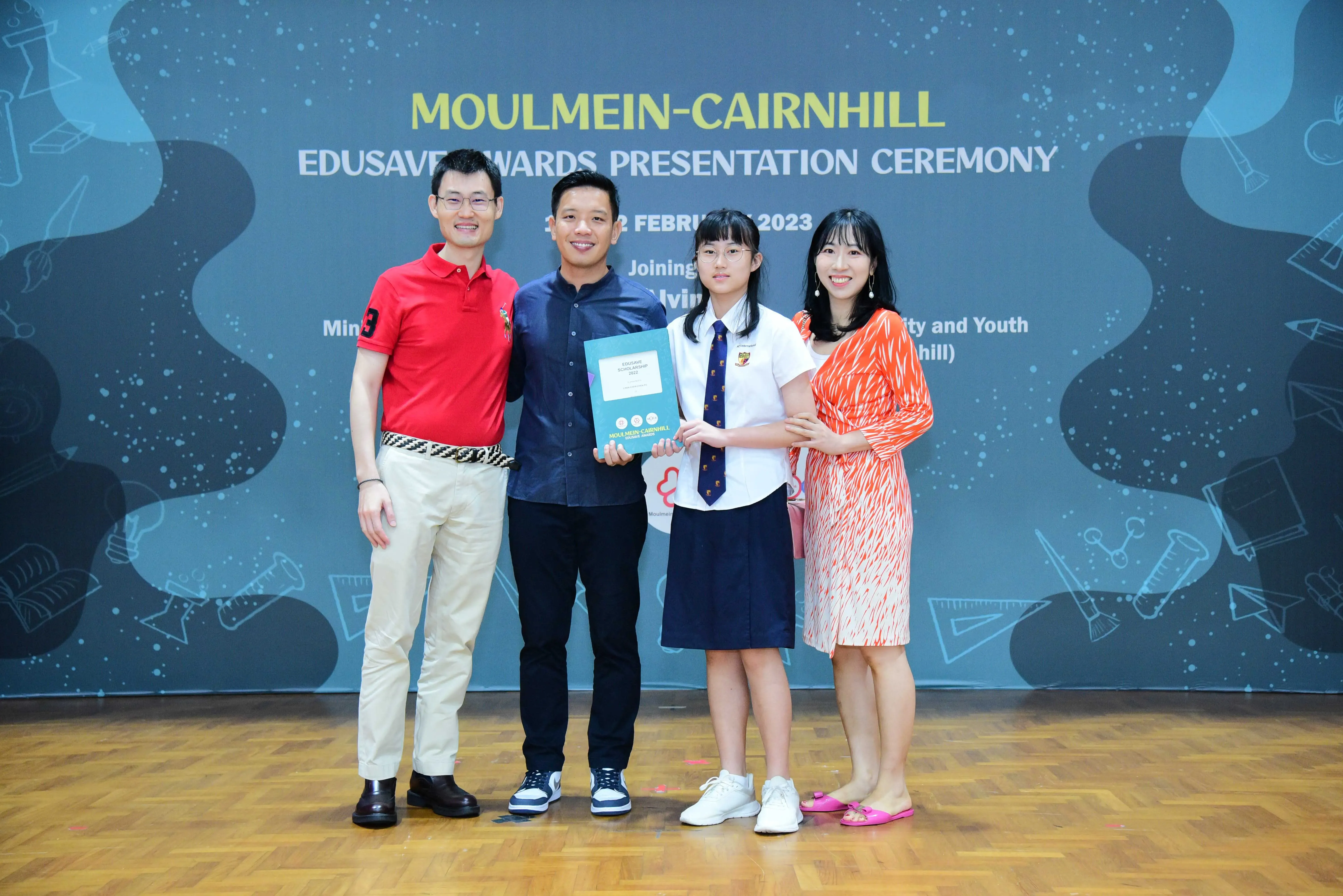 Four people pose at the Moulmein-Cairnhill Edusave Awards Presentation Ceremony, with a student holding a certificate.