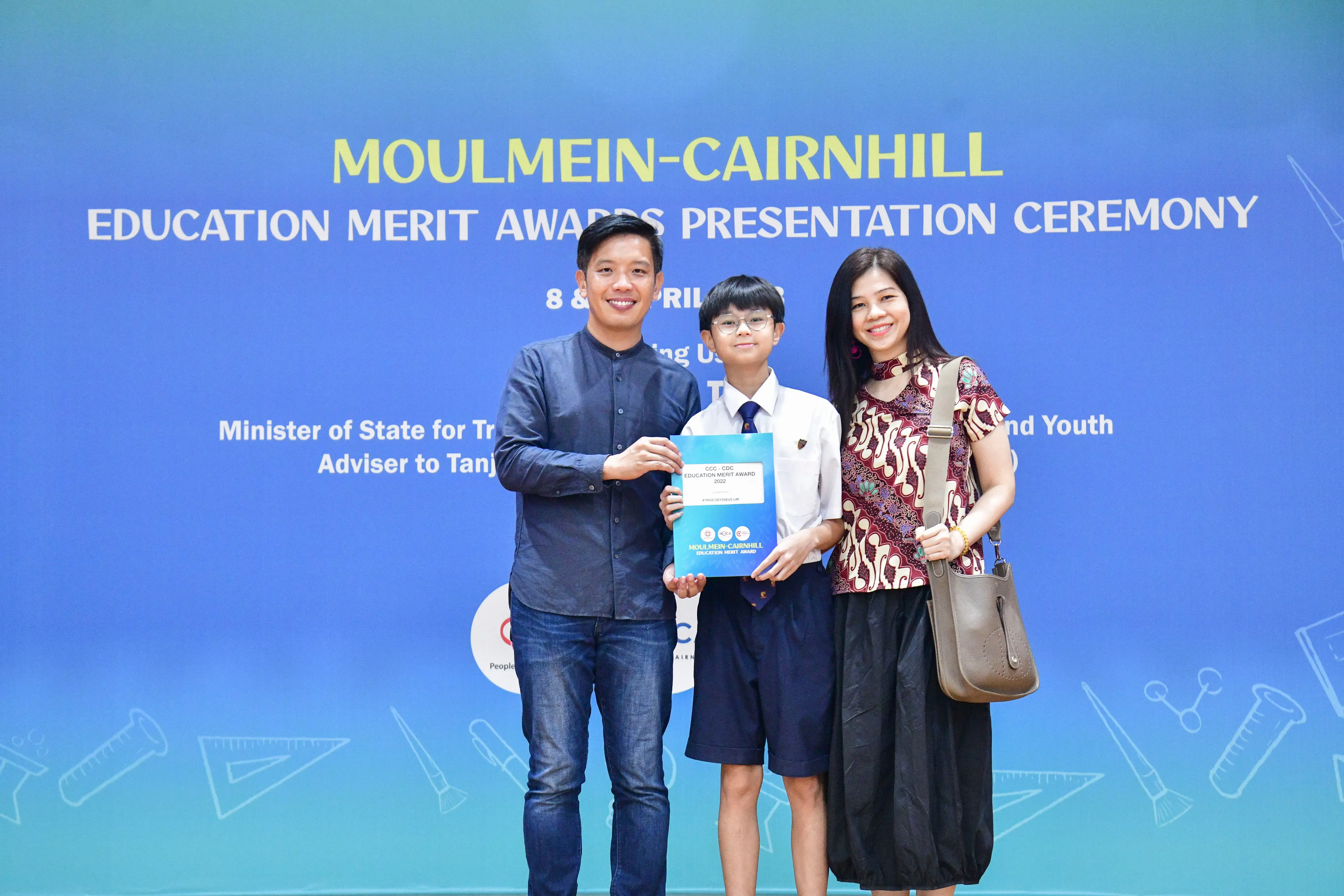 Three people pose holding an award folder at the Moulmein-Cairnhill Education Merit Awards Presentation Ceremony.