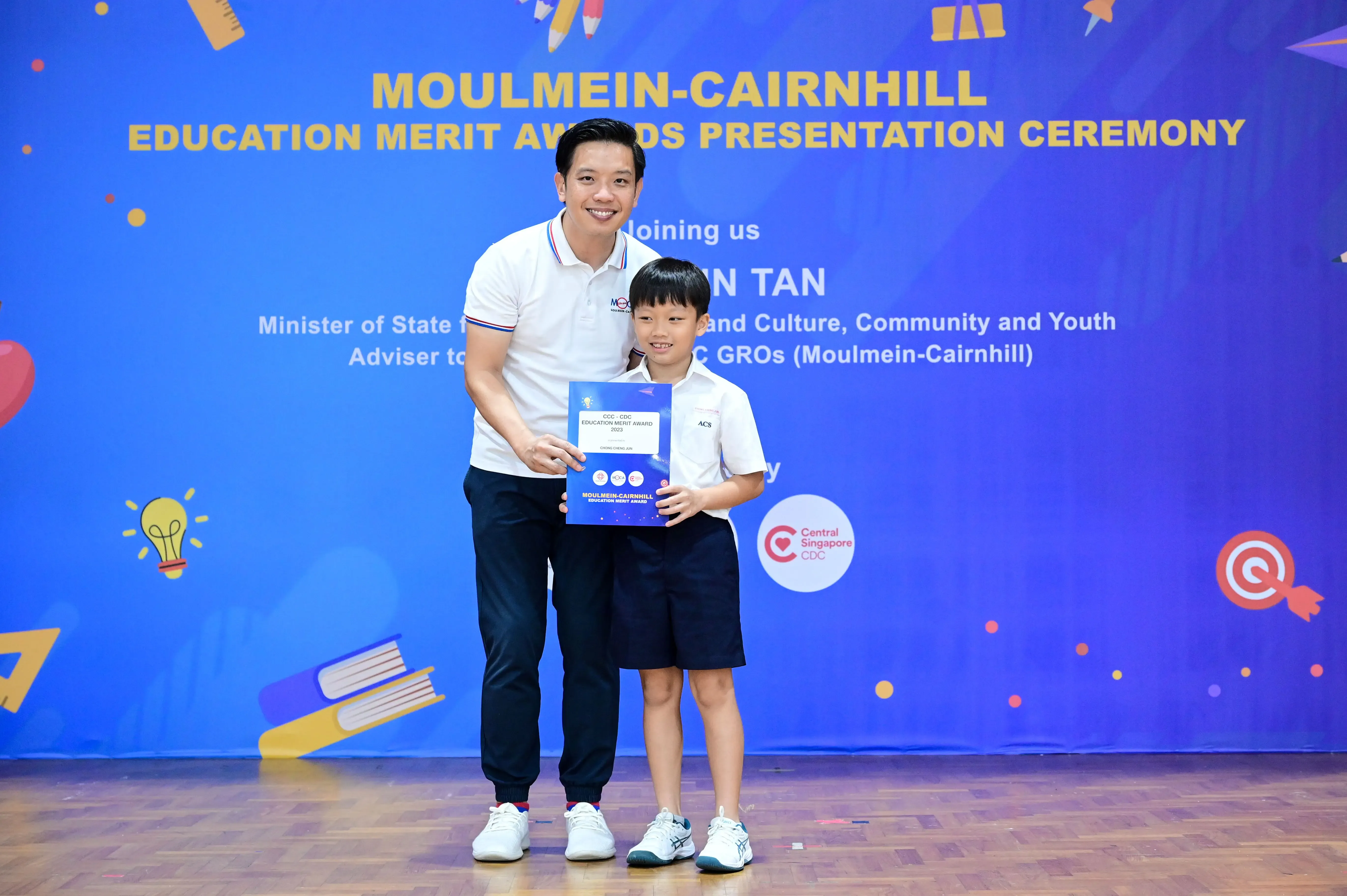A man and a young boy hold a certificate at the Moulmein-Cairnhill Education Merit Awards Presentation Ceremony.