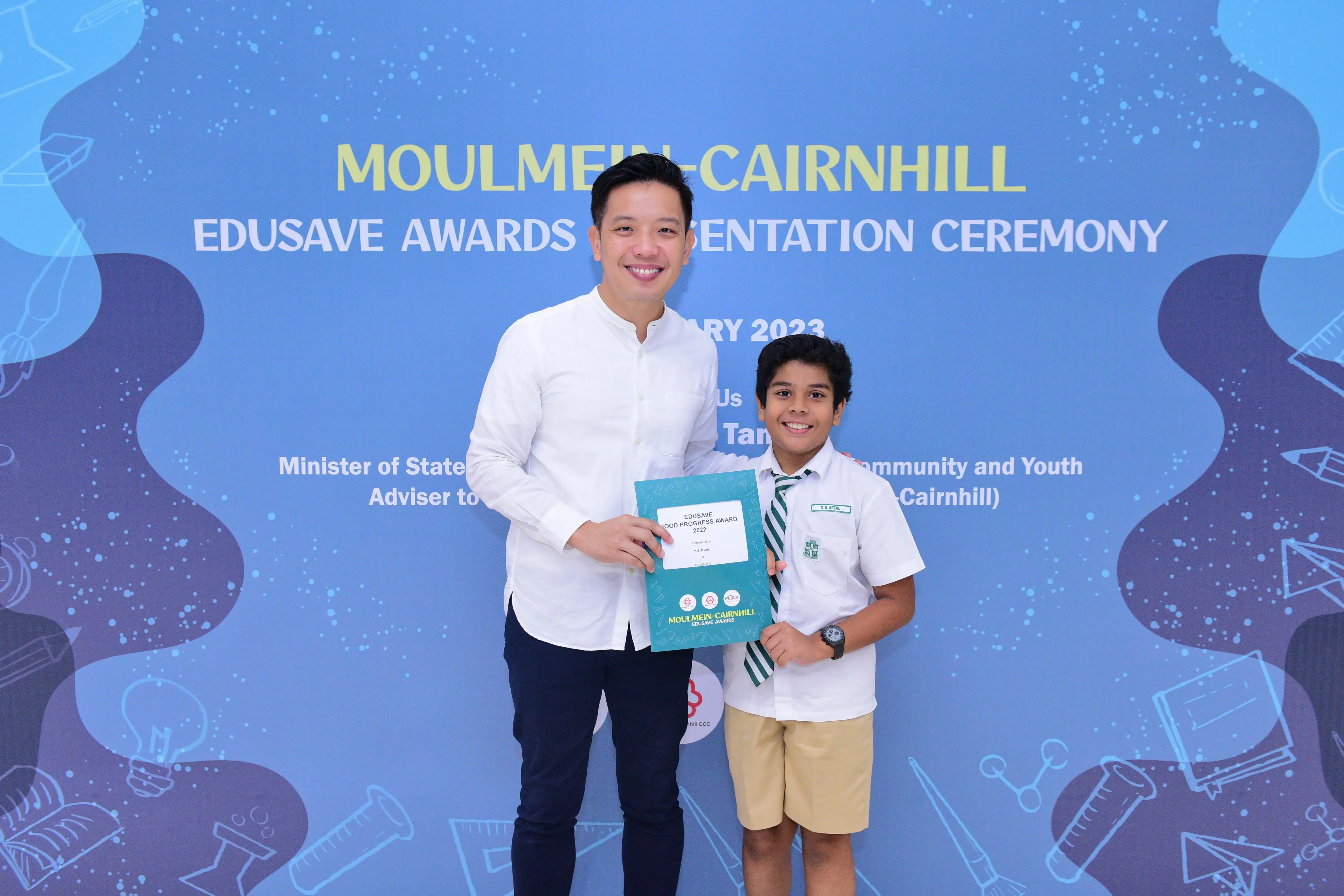 Adult and young student in school uniform hold a certificate at the Moulmein-Cairnhill Edusave Awards Ceremony 2023.
