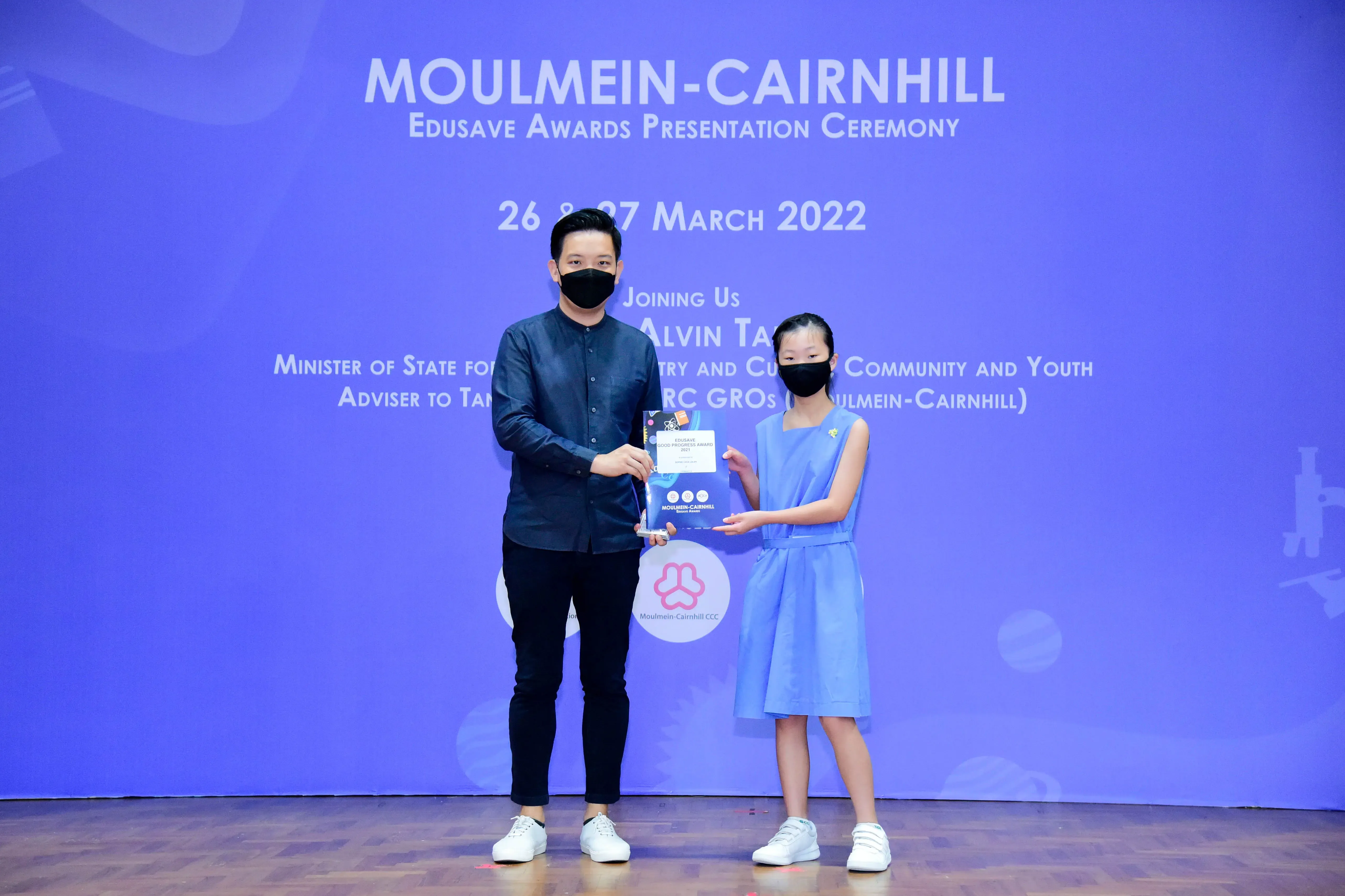 A man and a young girl in masks hold an award together at the Moulmein-Cairnhill Edusave Awards Ceremony 2022.