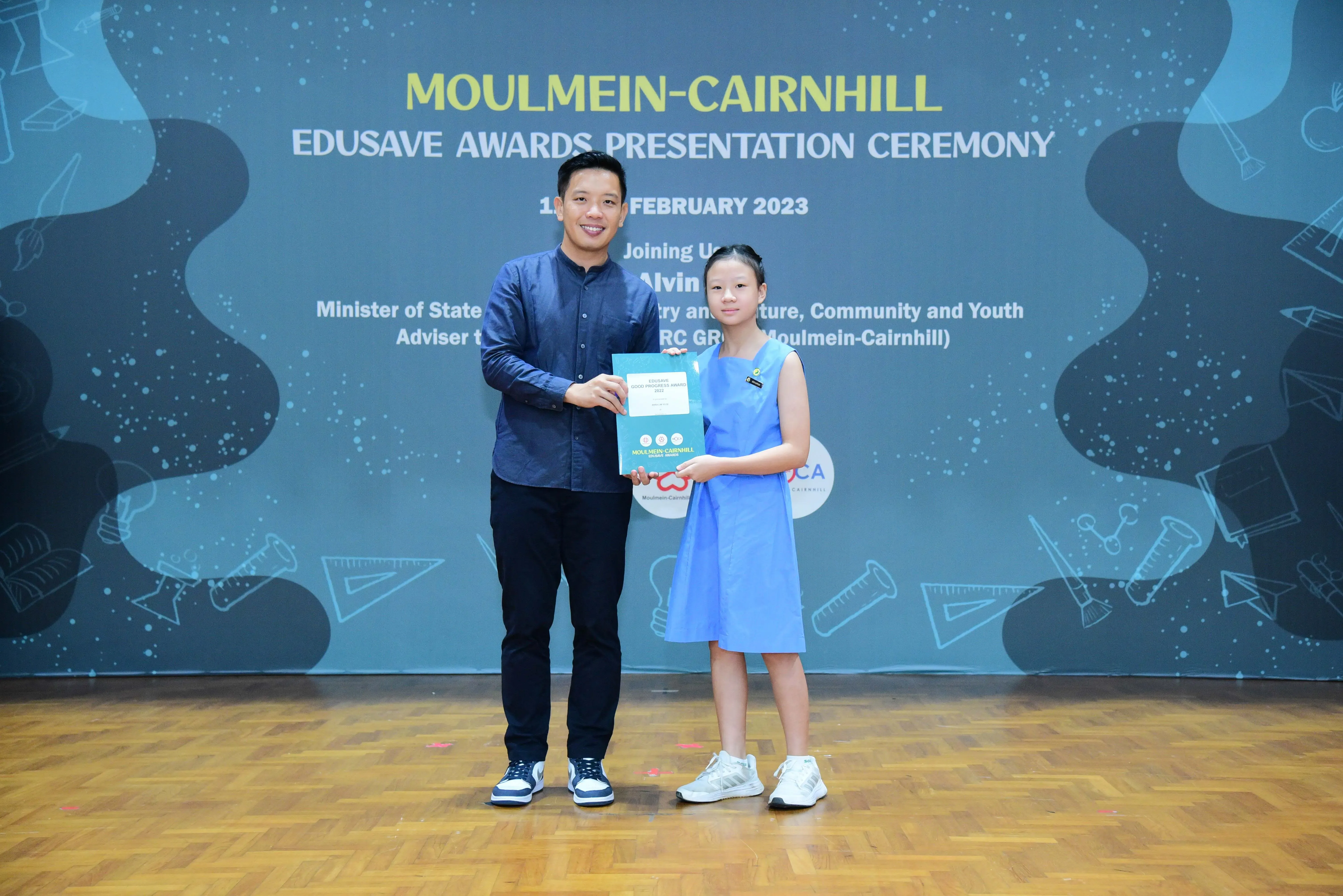 A man and a young girl hold an award booklet at the Moulmein-Cairnhill Edusave Awards Ceremony, February 2023.