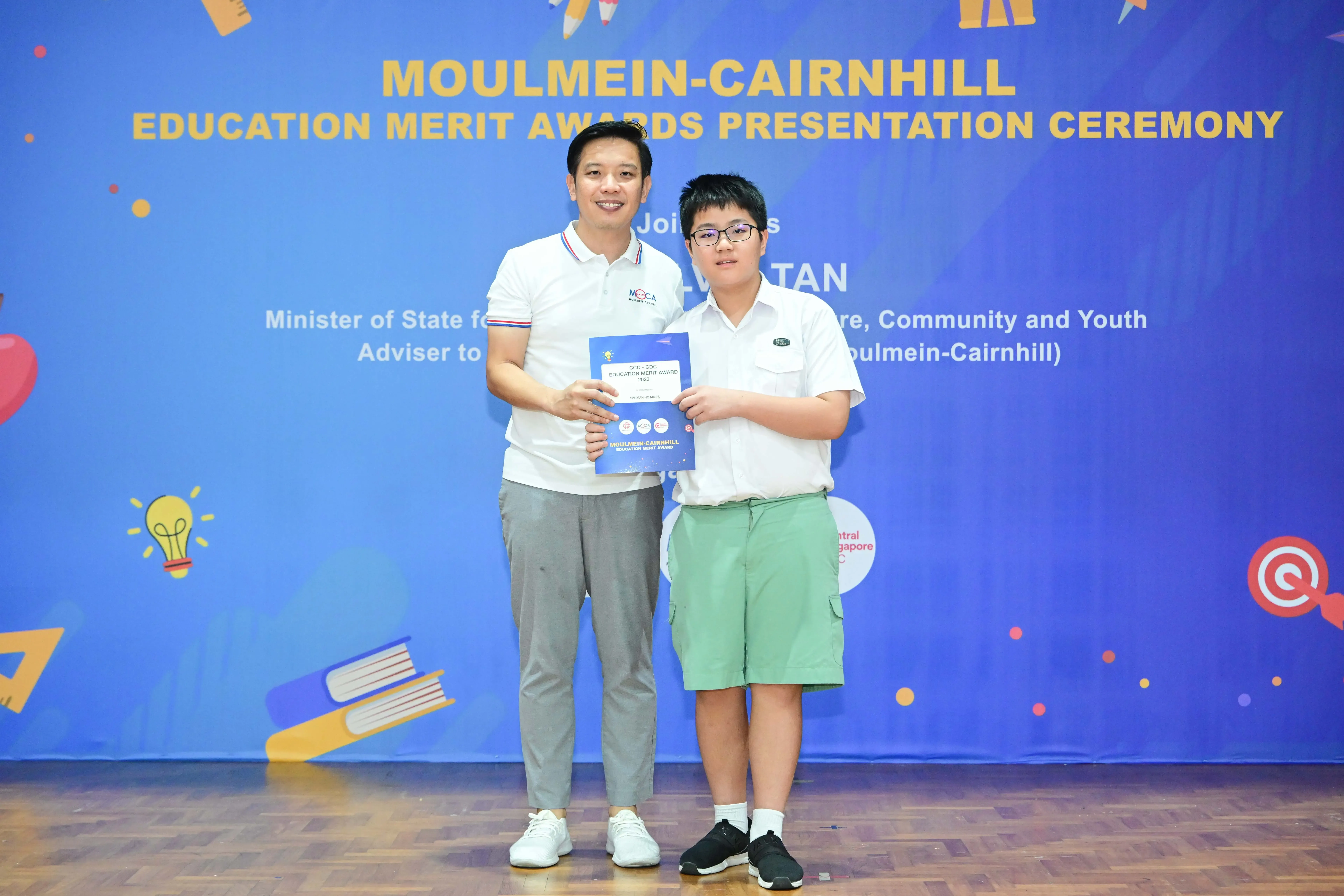 Two people hold a certificate at the Moulmein-Cairnhill Education Merit Awards Presentation Ceremony.