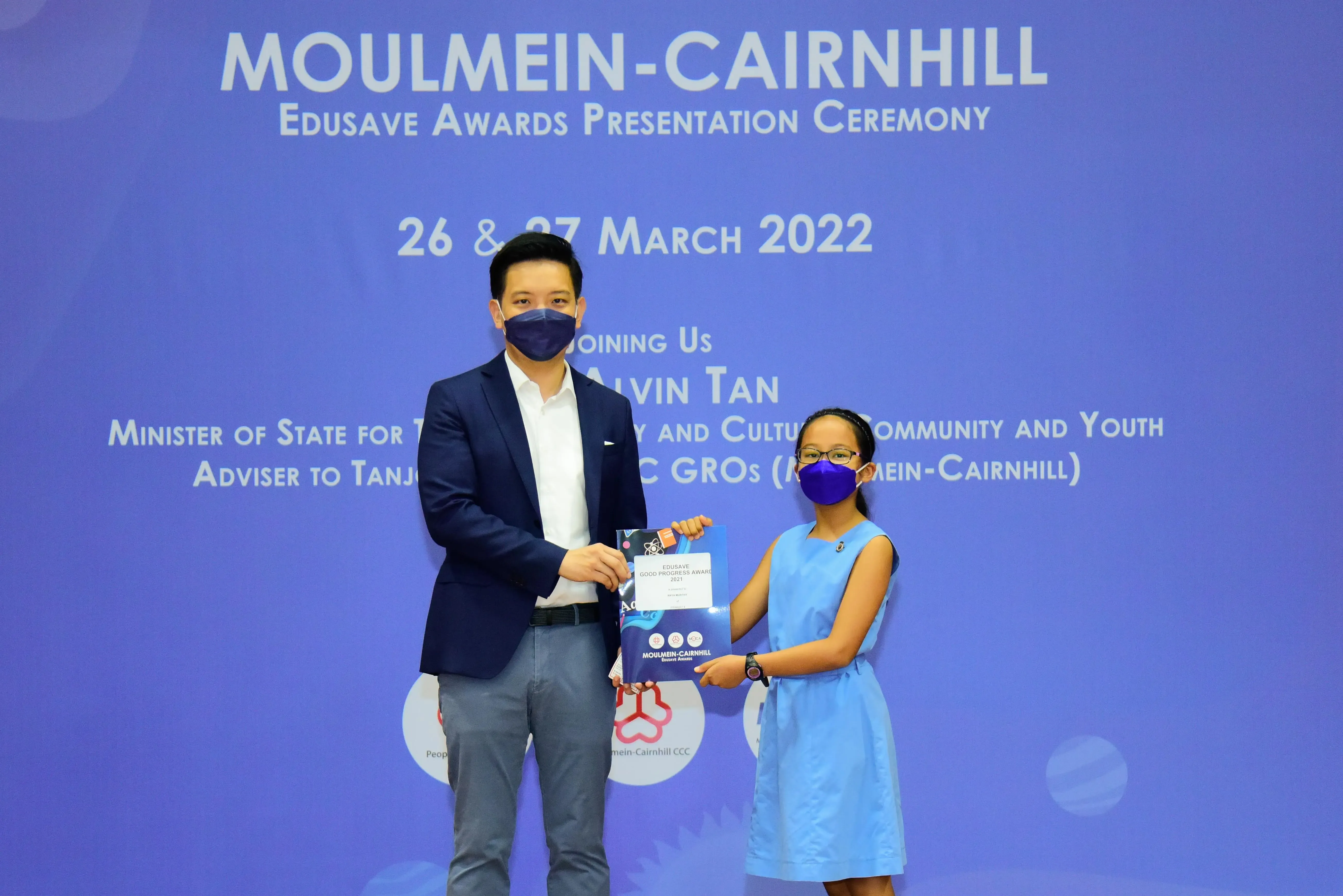 A man and a young girl in masks hold an award certificate at the Moulmein-Cairnhill Edusave Awards Ceremony, March 2022.