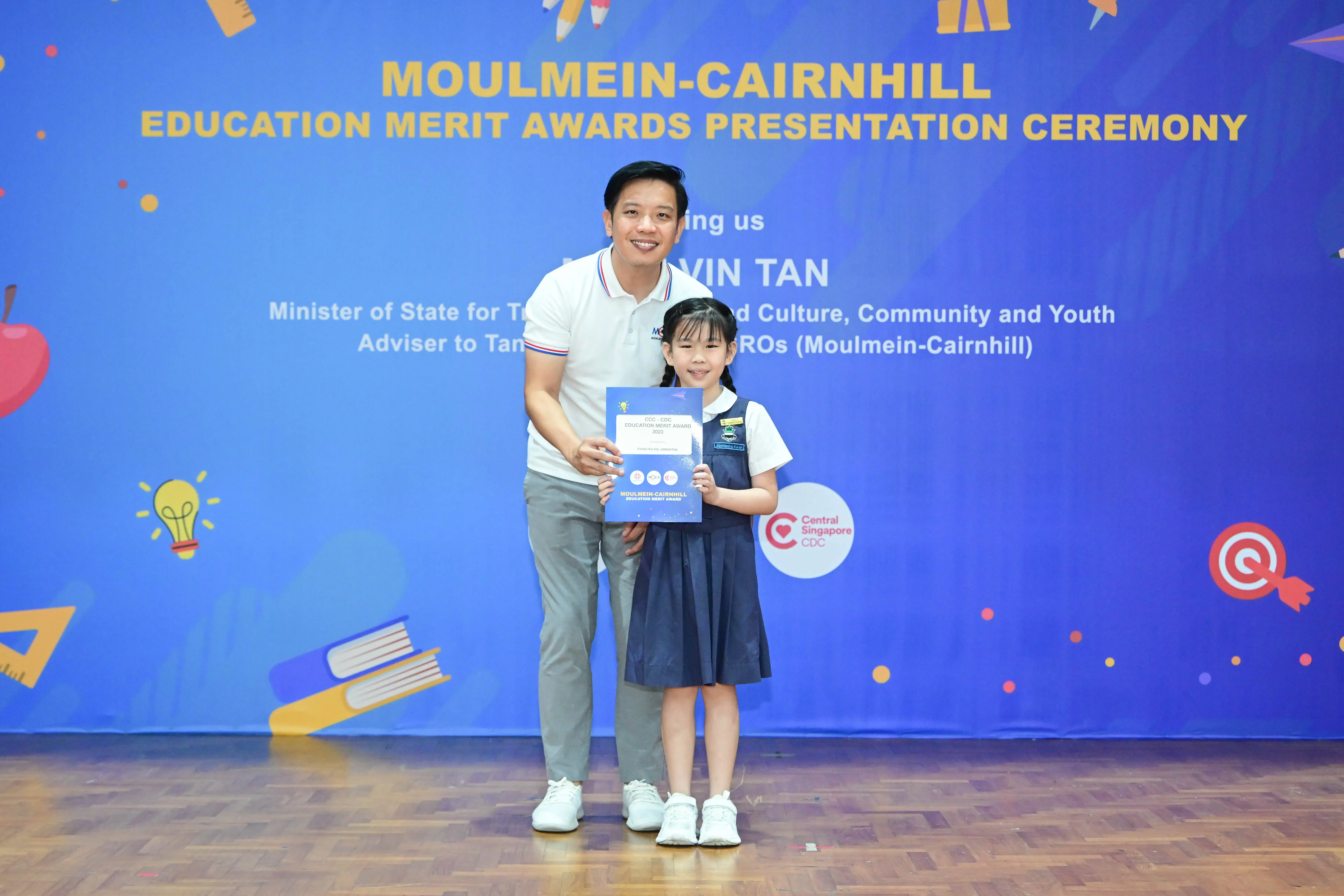 A man and a young girl in school uniform hold a certificate at the Moulmein-Cairnhill Education Merit Awards ceremony.