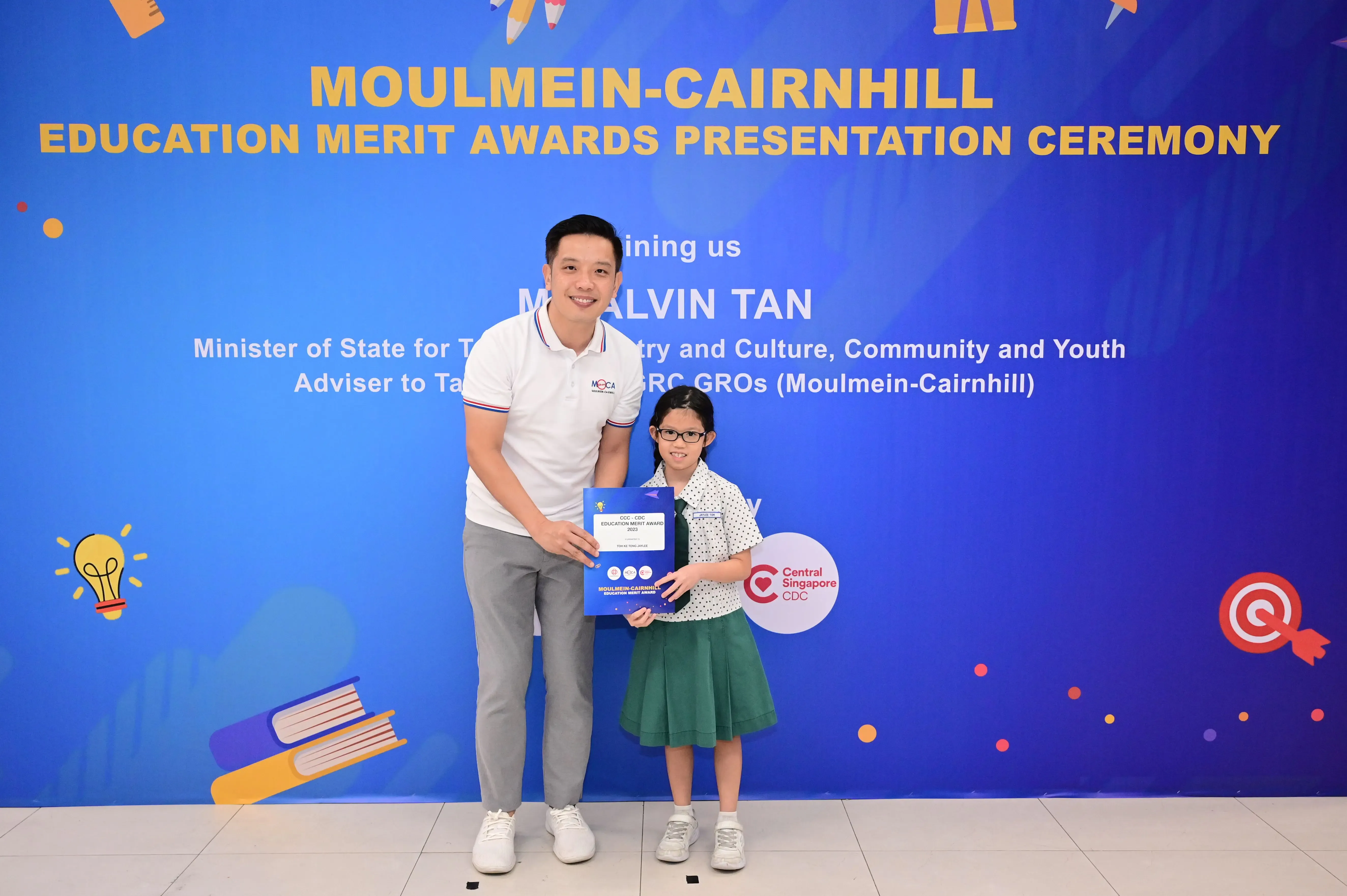 A man and a young girl hold an award certificate at the Moulmein-Cairnhill Education Merit Awards Presentation Ceremony.