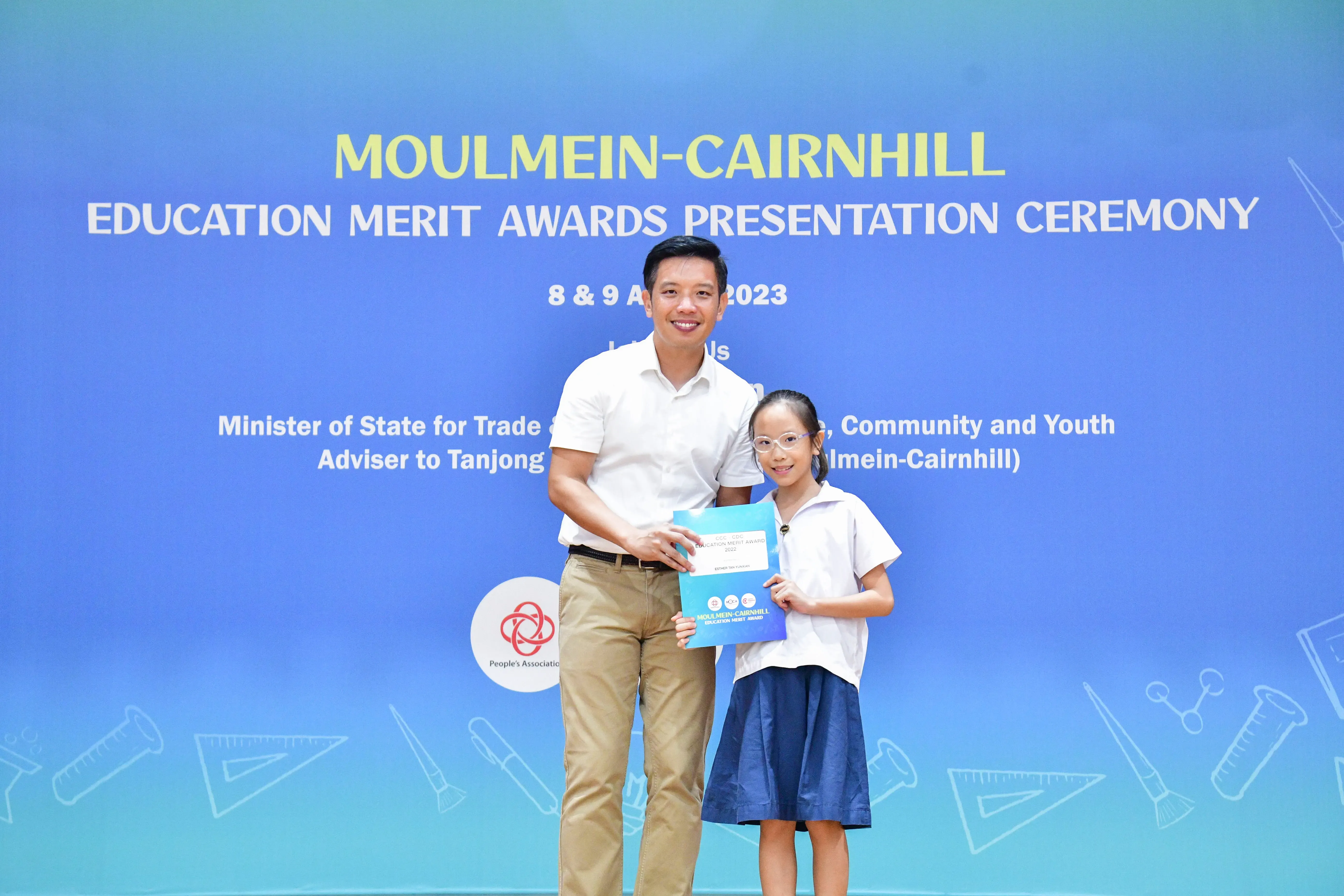 A man and a young girl hold an award certificate at the Moulmein-Cairnhill Education Merit Awards Ceremony 2023.