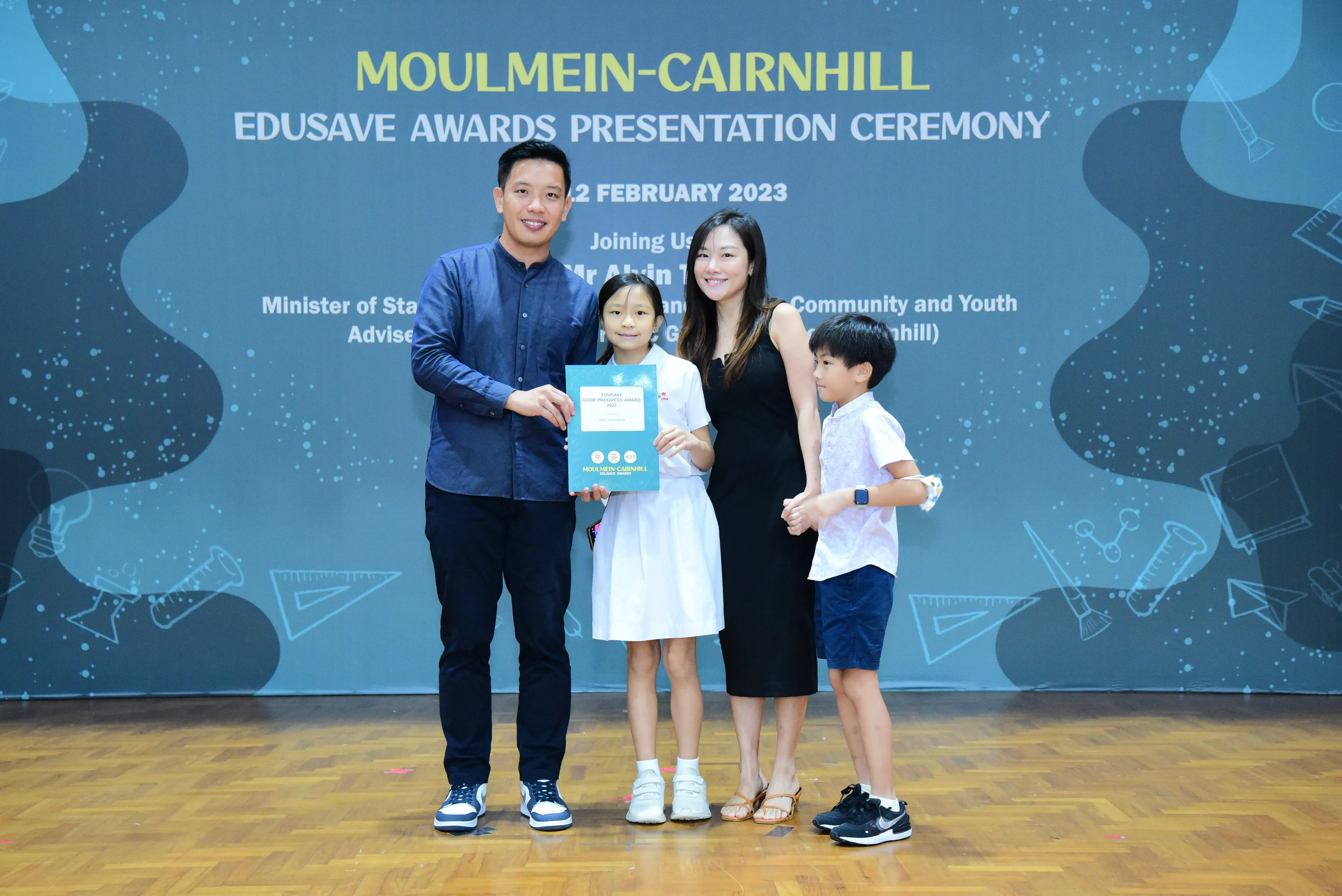 Family of four posing with an award certificate at the Moulmein-Cairnhill Edusave Awards Ceremony in February 2023.