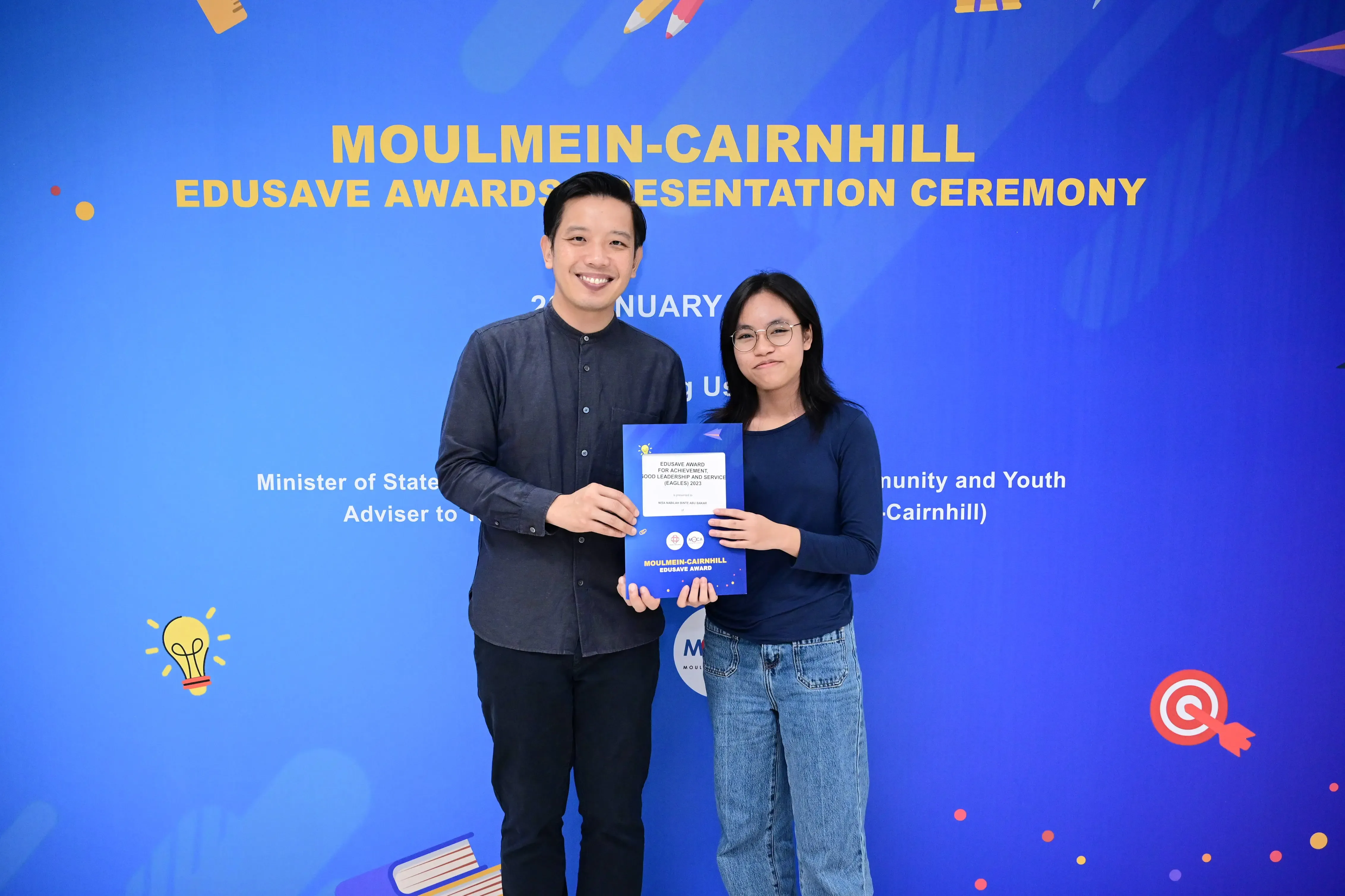 Two people hold an award certificate together at the Moulmein-Cairnhill Edusave Awards Presentation Ceremony.