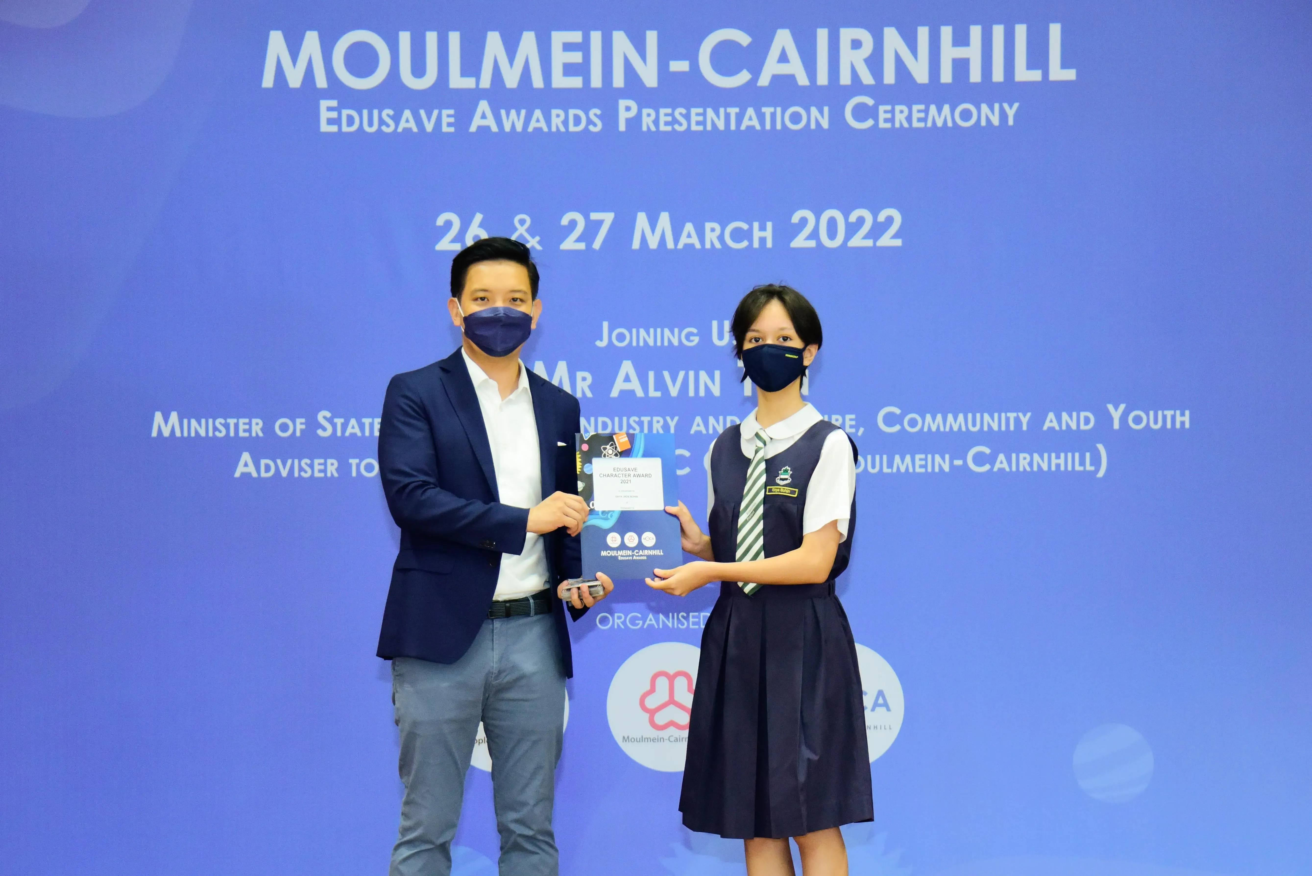 Two masked individuals hold an award certificate at the Moulmein-Cairnhill Edusave Awards Presentation Ceremony, March 2022.
