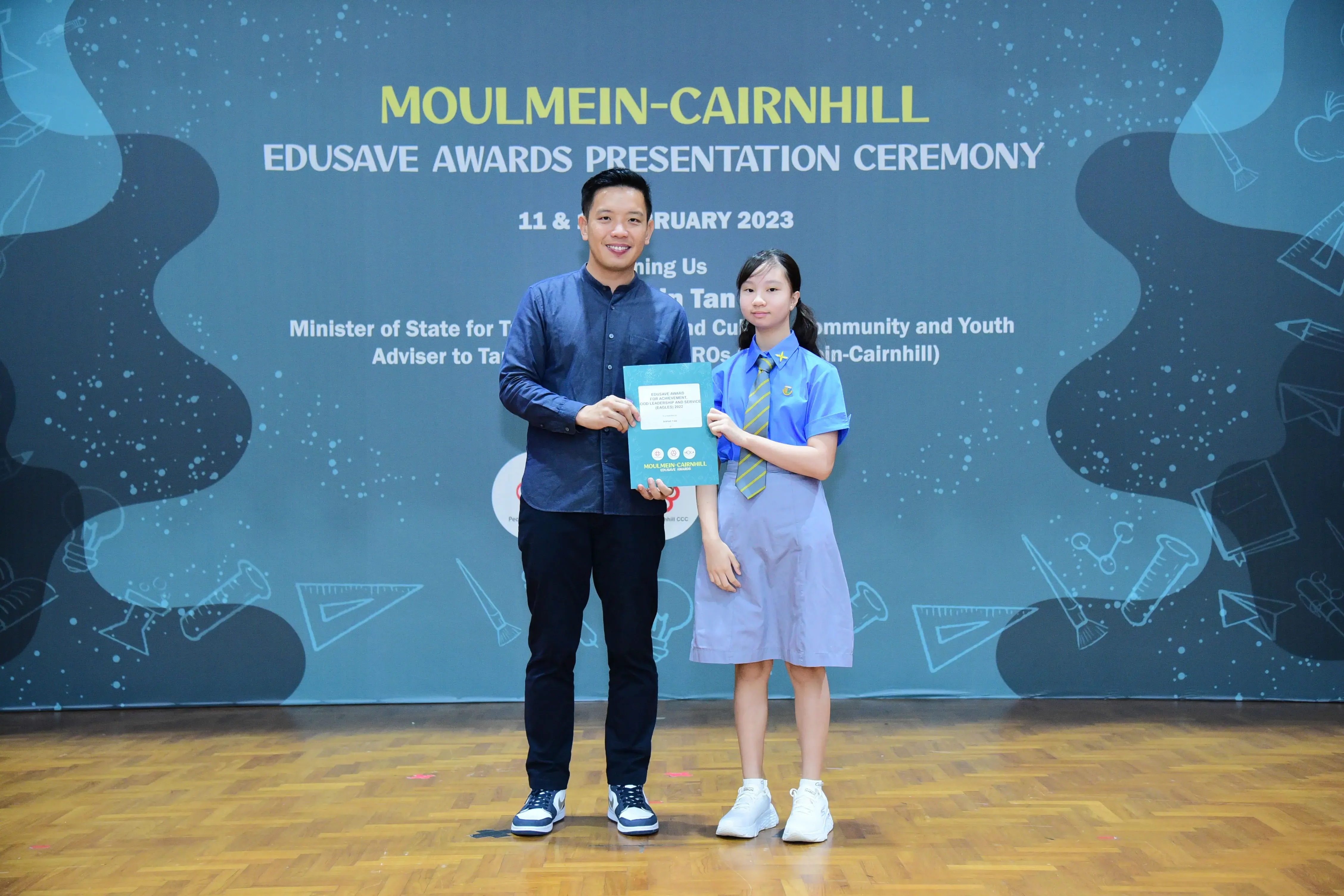 A man and a uniformed schoolgirl hold a certificate together at the Moulmein-Cairnhill Edusave Awards Ceremony 2023.