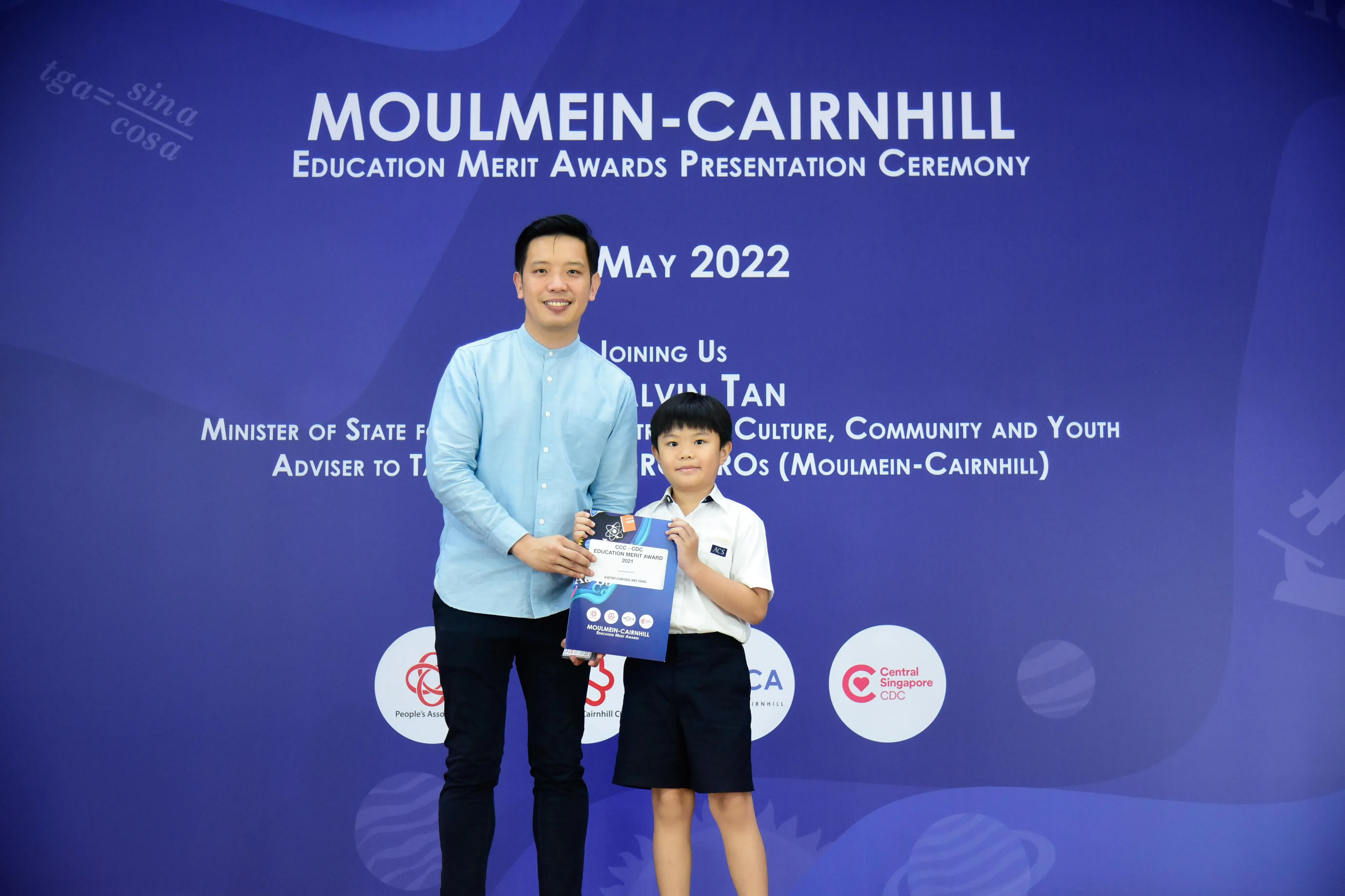 A man and a young boy hold an award certificate at the Moulmein-Cairnhill Education Merit Awards Ceremony, May 2022.