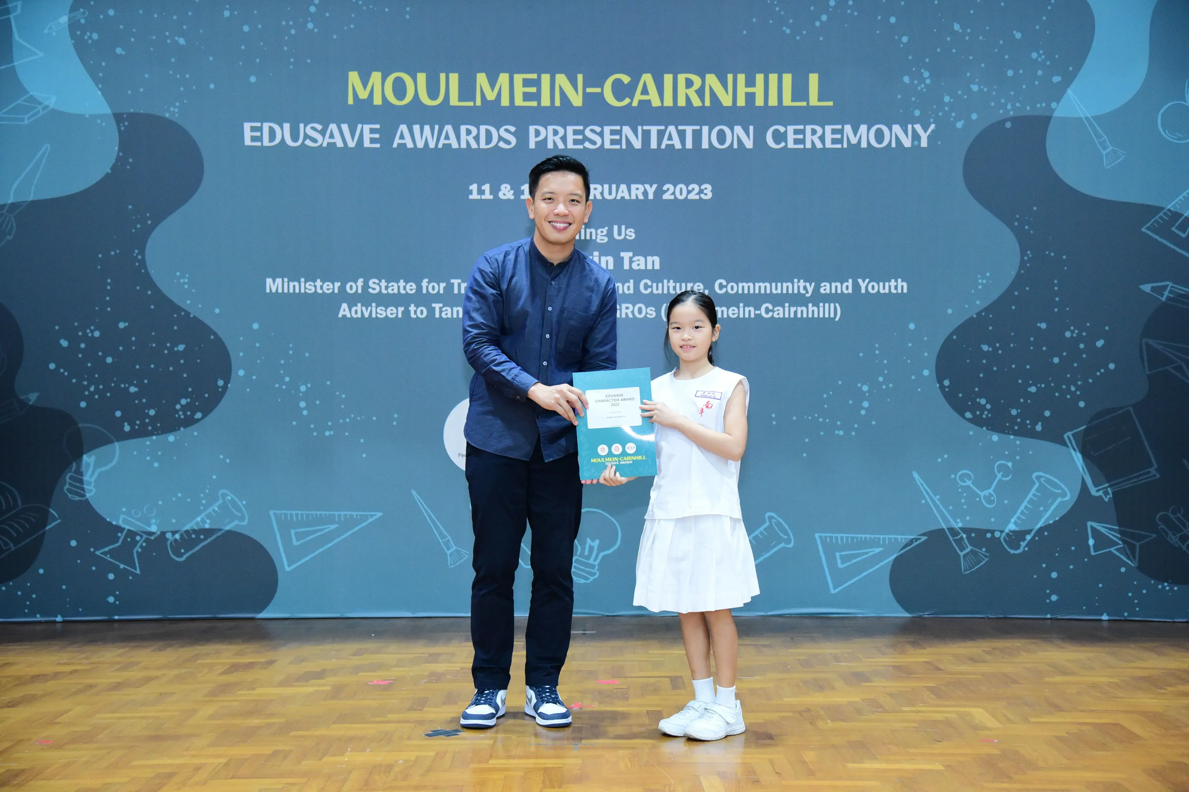 A man and a young girl hold a certificate together at the Moulmein-Cairnhill Edusave Awards Ceremony in 2023.
