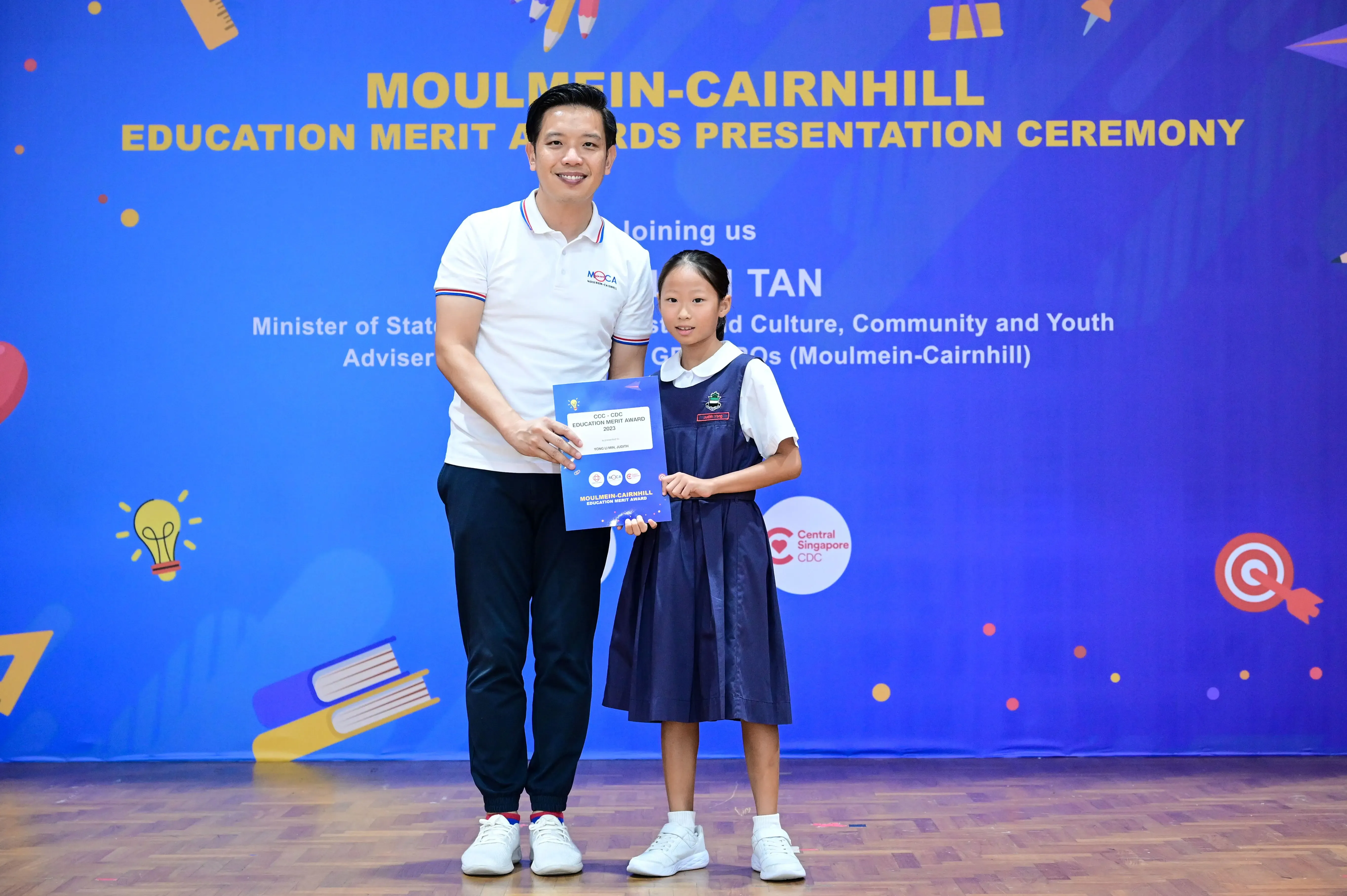 A man and a young girl in school uniform hold a certificate at the Moulmein-Cairnhill Education Merit Awards ceremony.