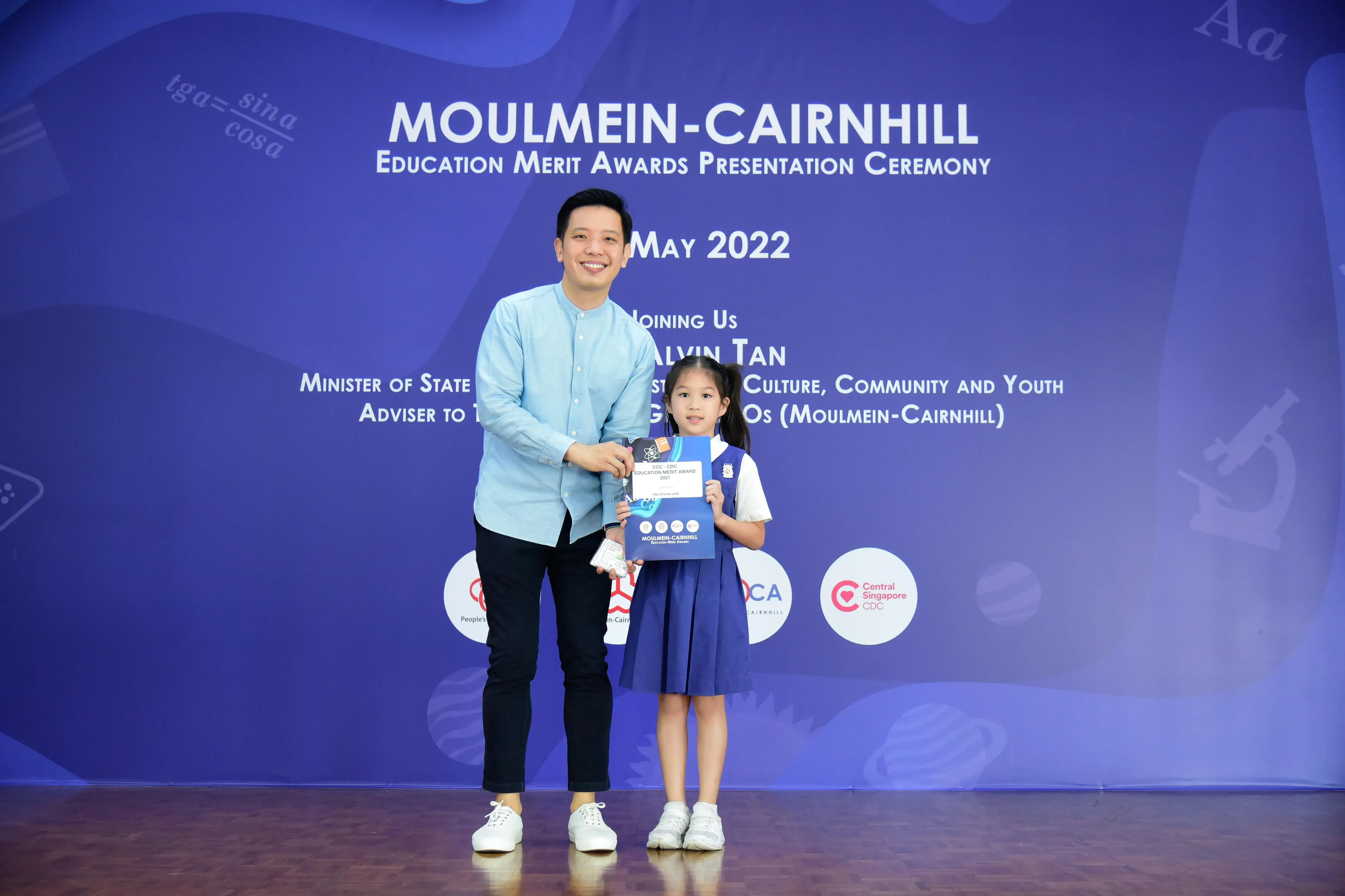 A man and a young girl in school uniform hold an award at the Moulmein-Cairnhill Education Merit Awards May 2022.