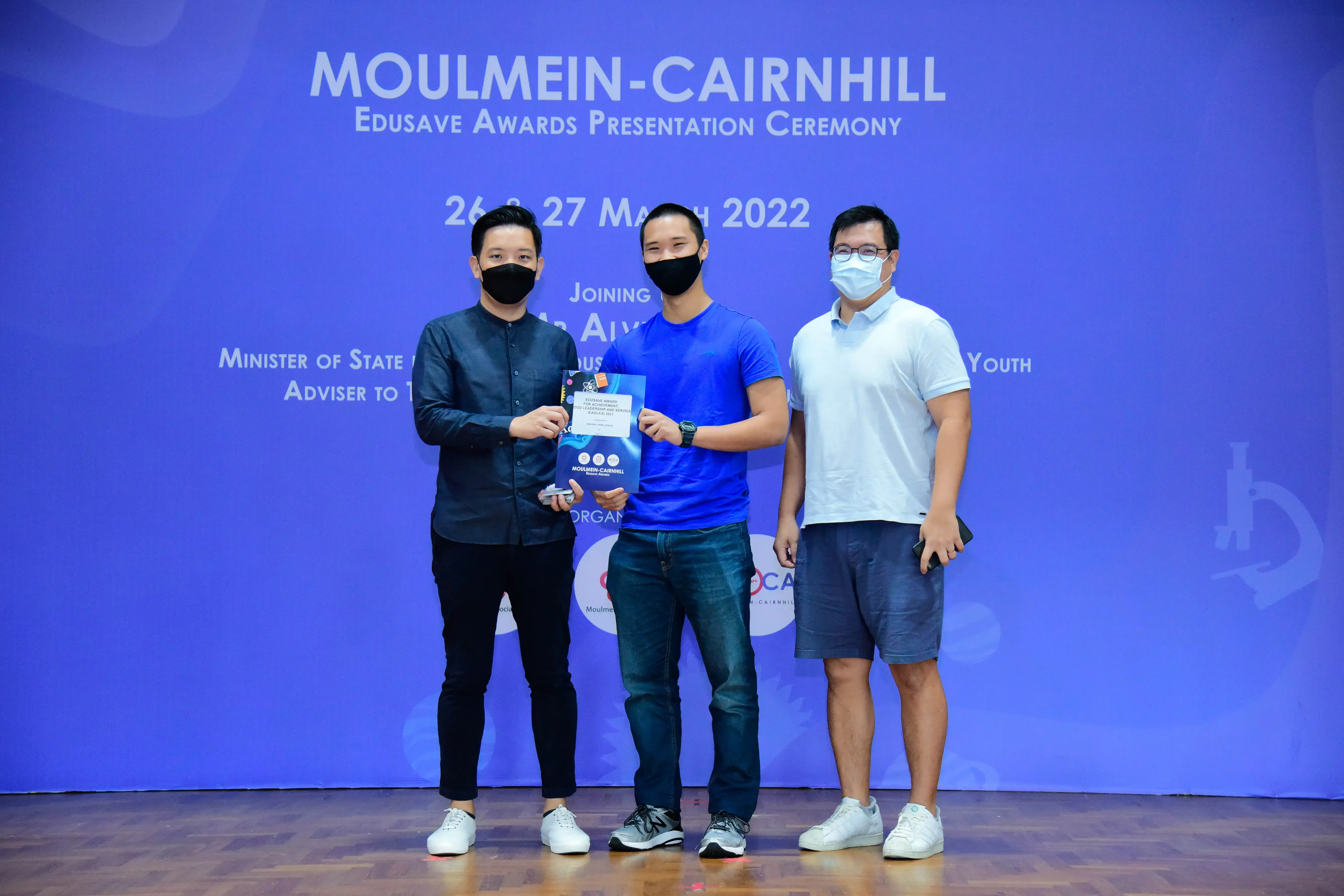 Three masked men pose on stage at the Moulmein-Cairnhill Edusave Awards Presentation Ceremony, March 2022.