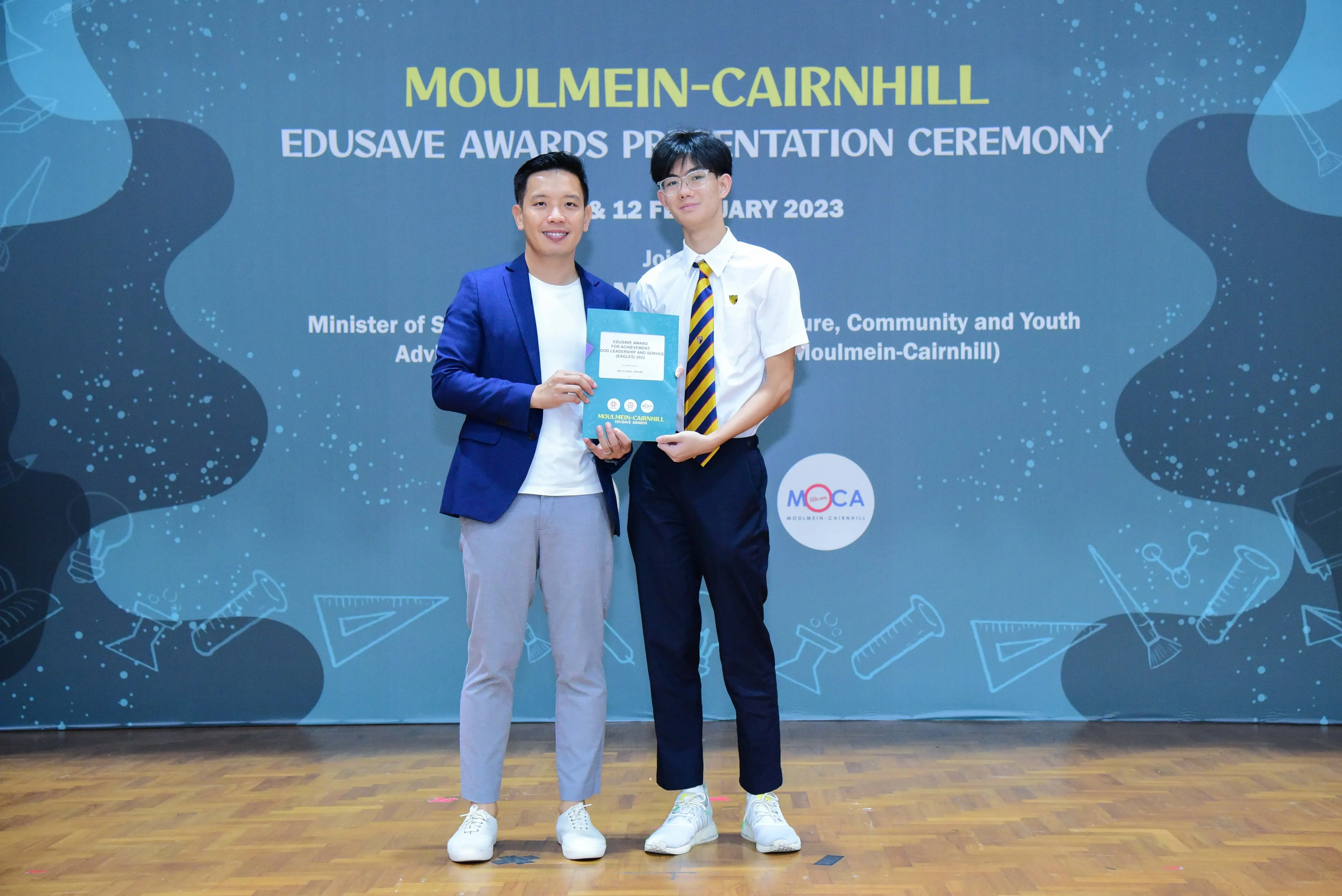 Two men hold a certificate at the Moulmein-Cairnhill Edusave Awards Presentation Ceremony in February 2023.