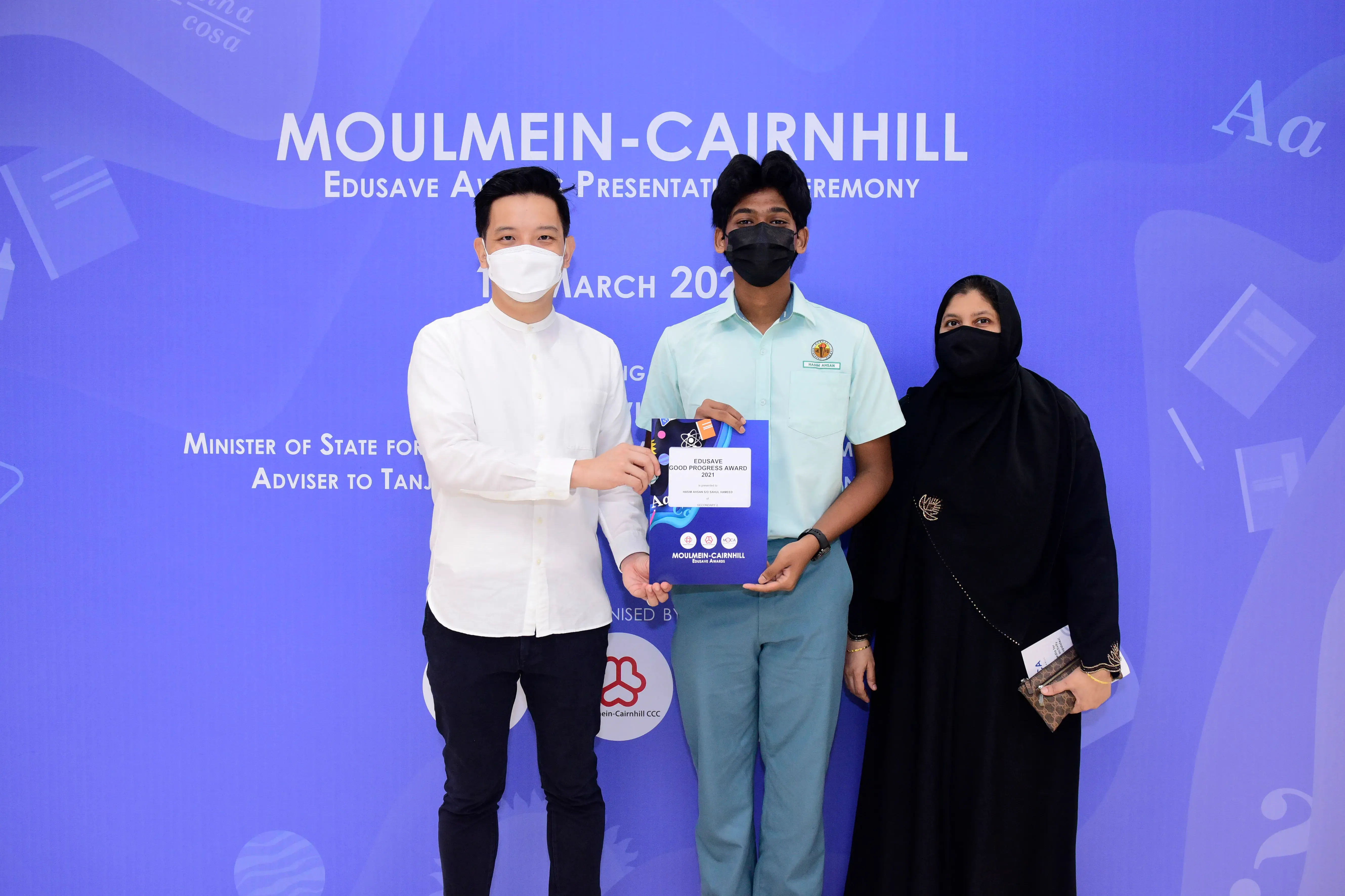 Three masked people pose at the Moulmein-Cairnhill Edusave Award Presentation Ceremony, holding an award certificate.