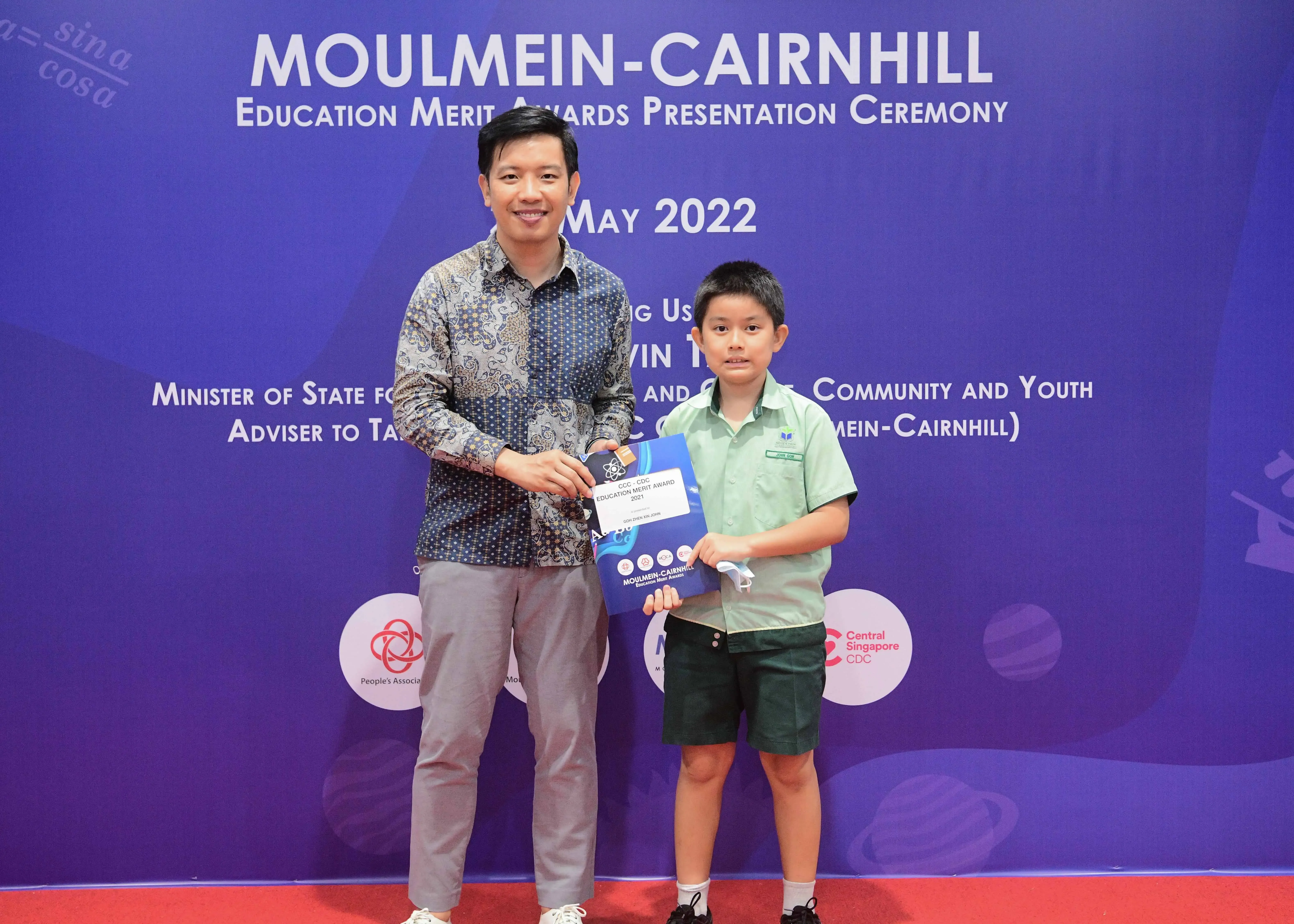 A man and a young boy hold an award certificate at the Moulmein-Cairnhill Education Merit Awards Ceremony, May 2022.