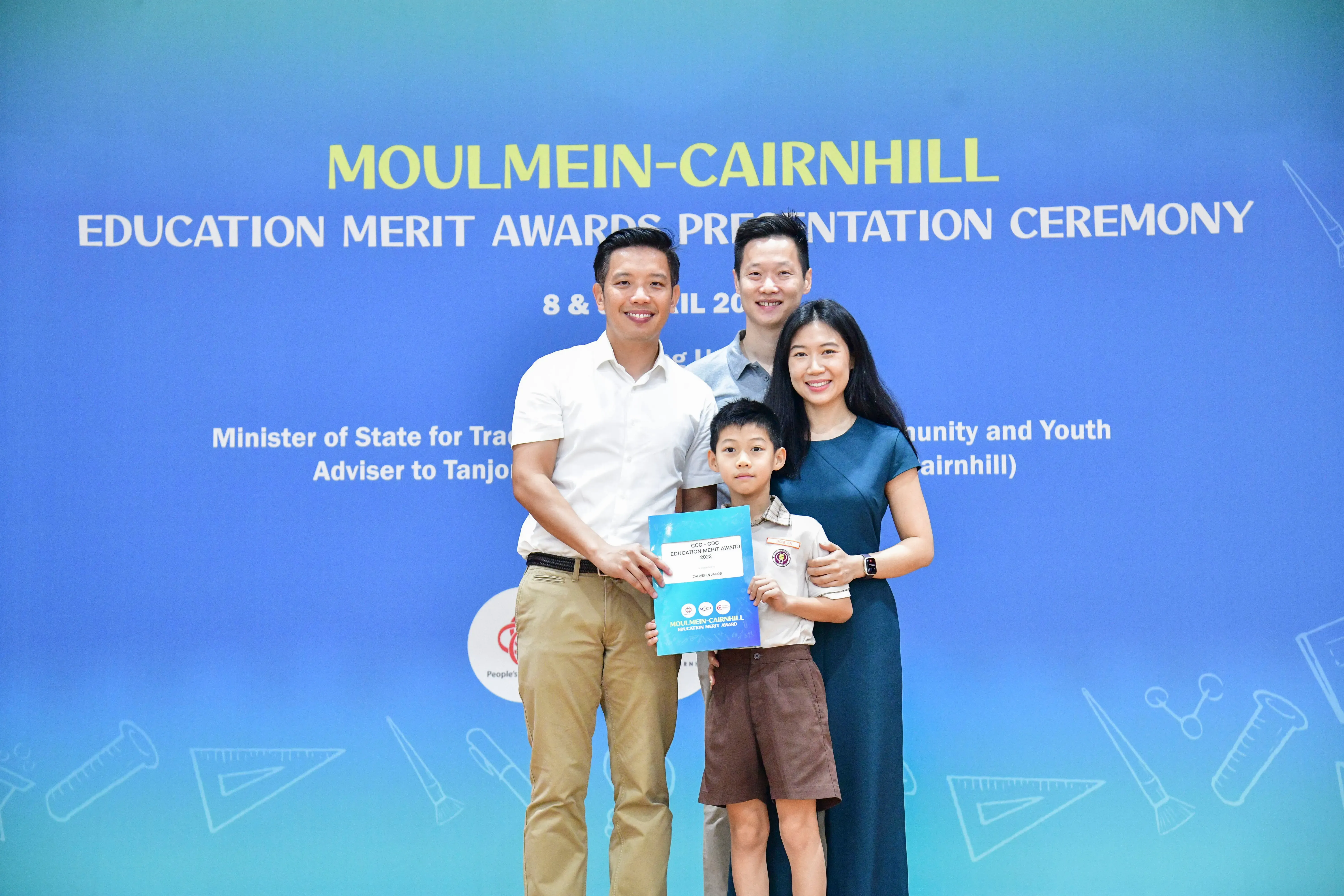 Three adults and a young boy pose with an award certificate at the Moulmein-Cairnhill Education Merit Awards Ceremony.